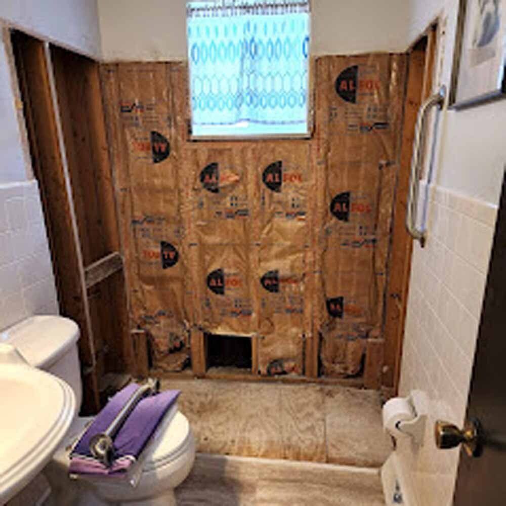 Partially renovated bathroom with exposed wall insulation and unfinished shower area