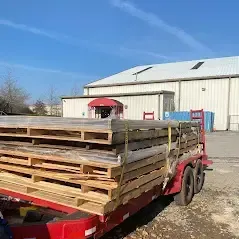 A red trailer filled with wooden pallets is parked in front of a building.