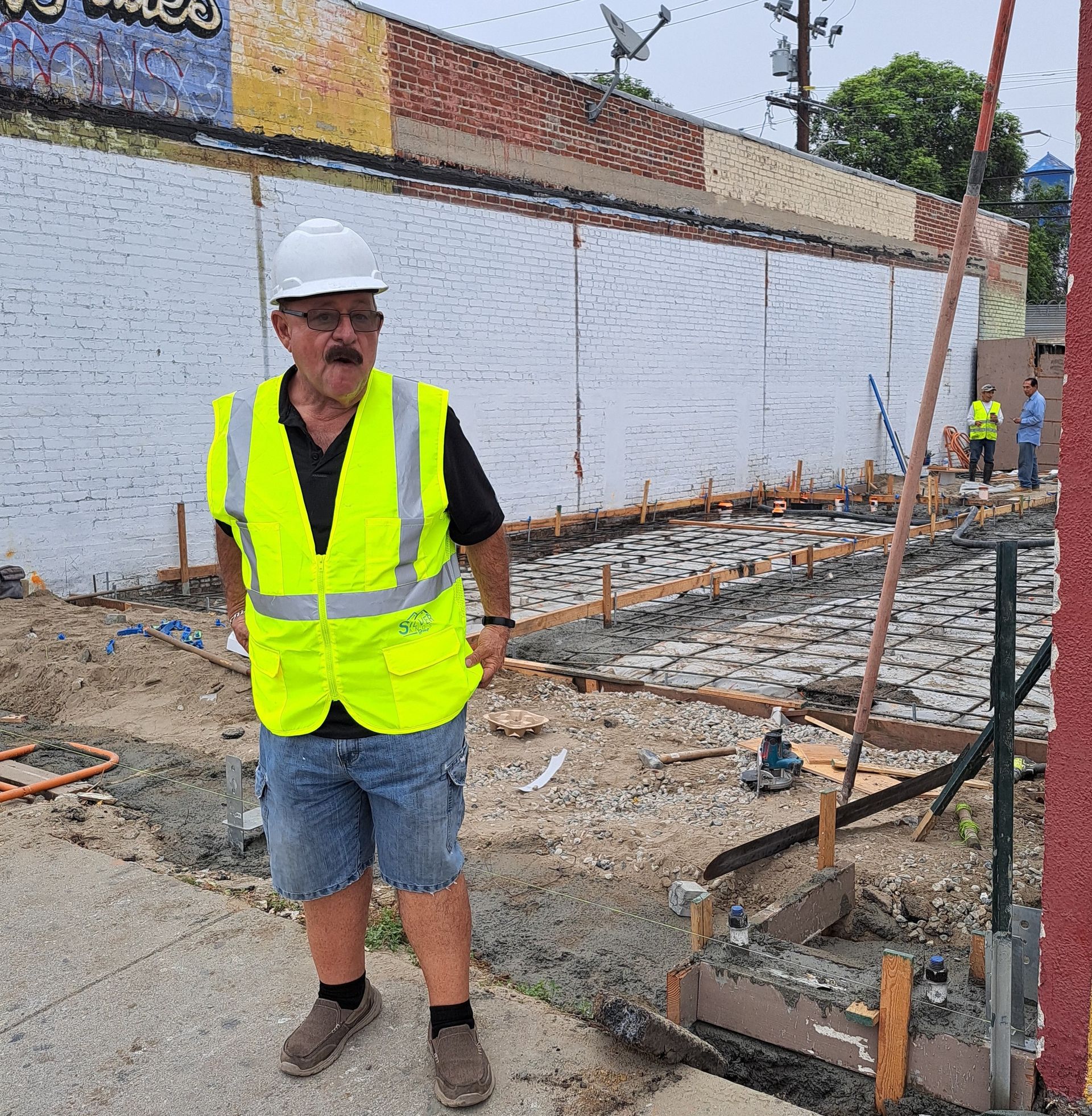 A man wearing a hard hat and safety vest is standing on a construction site.