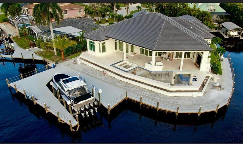 Aerial view of a waterfront house with a dock and parked boat beside blue water