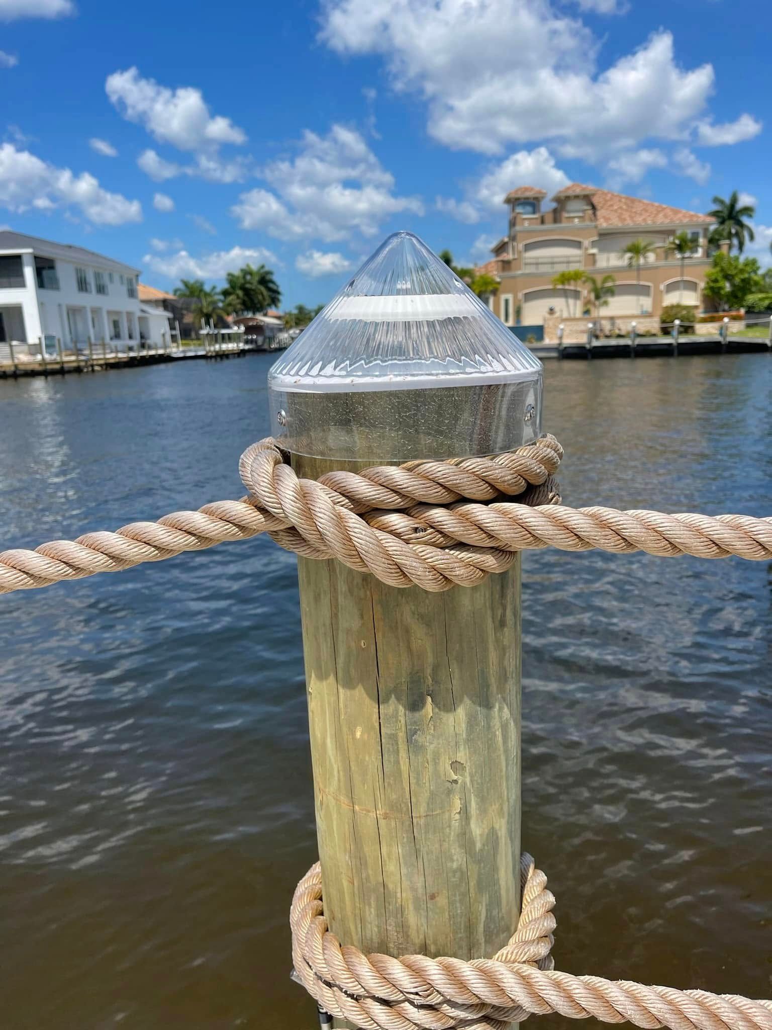 Tied wooden dock post with rope in calm water, with waterfront homes and blue sky in the background