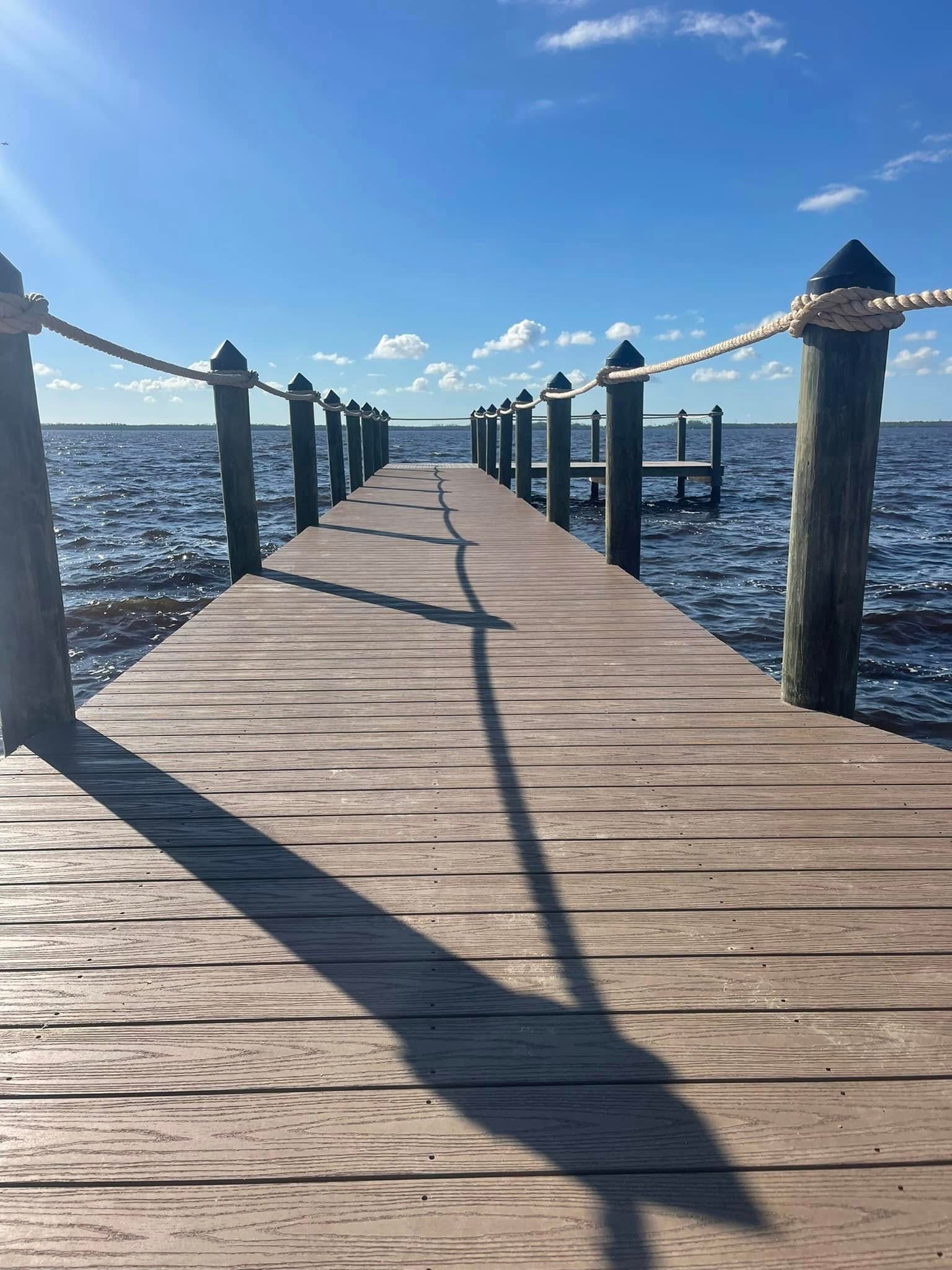 Wooden pier extending into sparkling blue water under a sunny sky, with posts and rope railings.