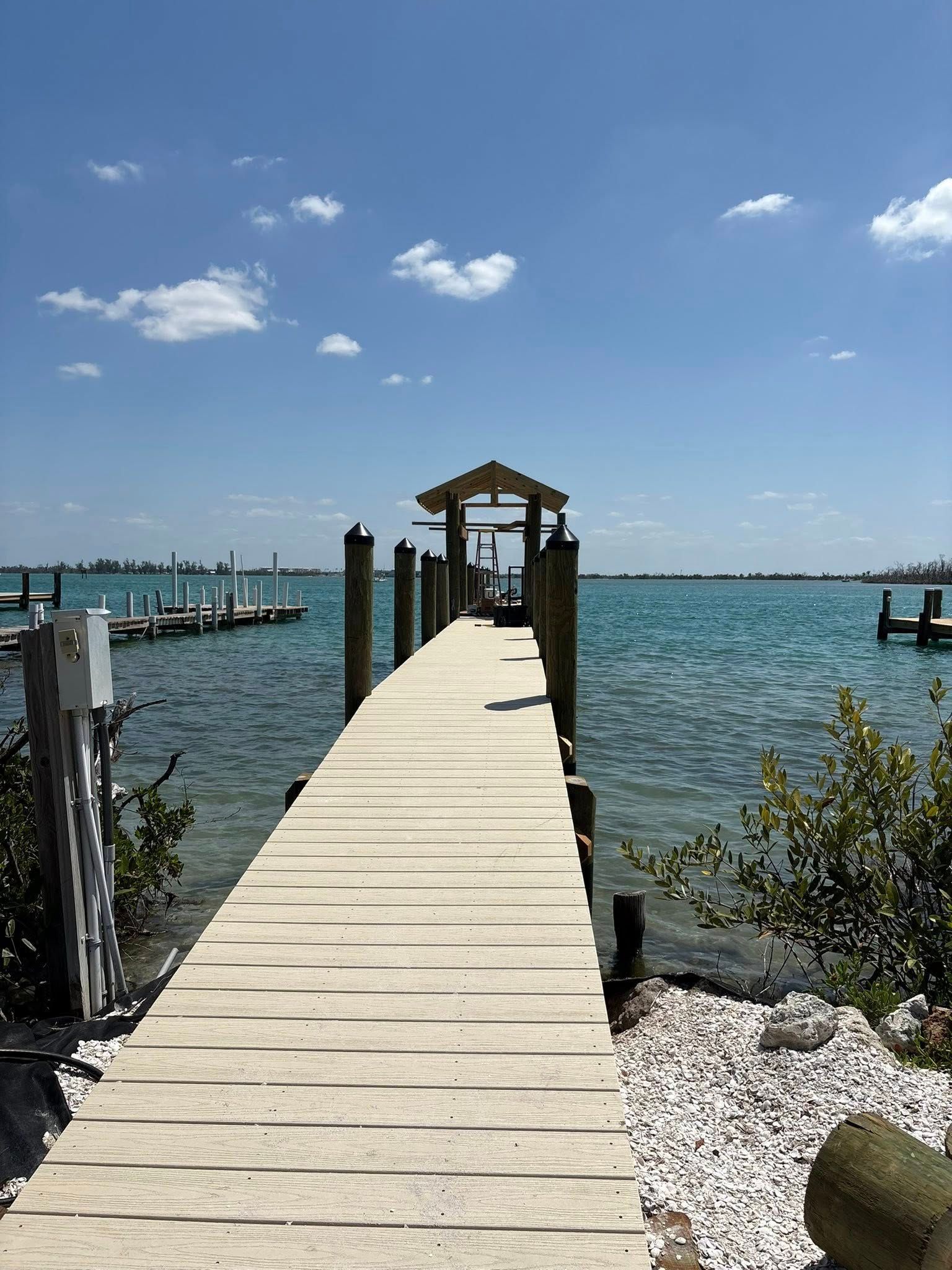 Wooden dock stretching into a blue bay under a sunny sky, with boats in the distance.