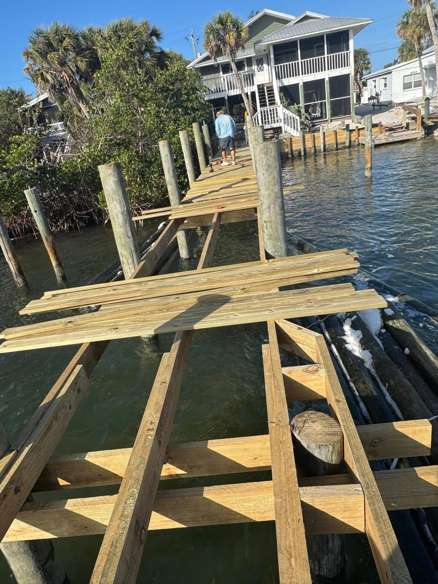 Wooden dock under construction over water beside a waterfront house and trees