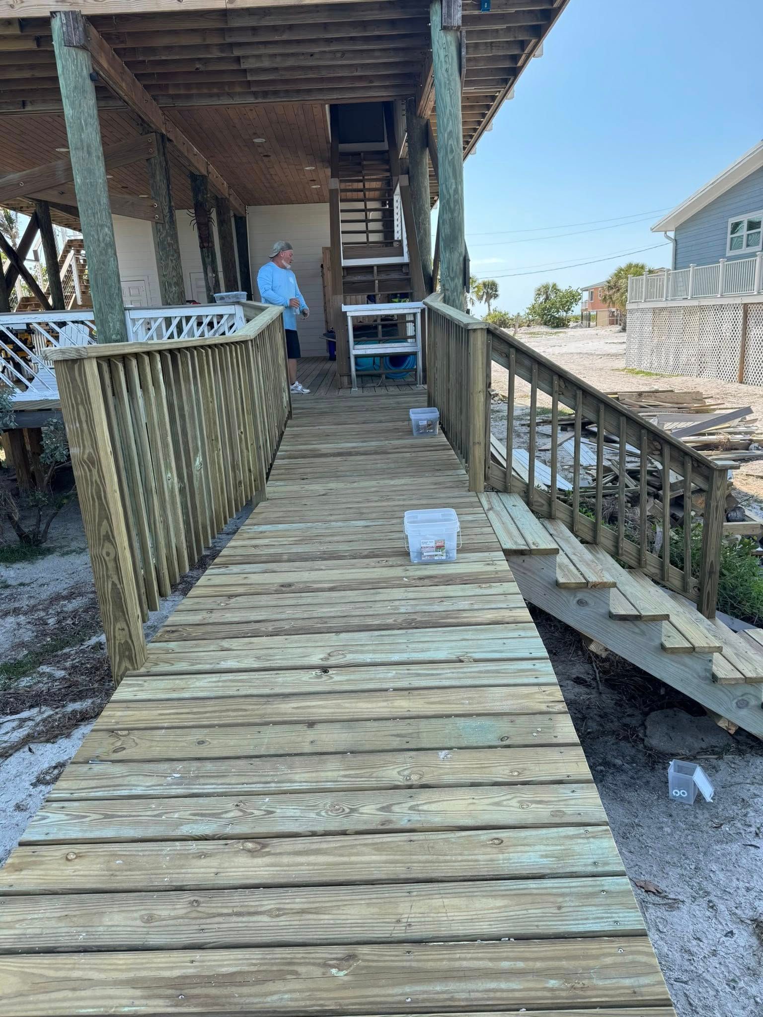 Wooden walkway leading to a porch under construction, with stairs and a person in a blue shirt.