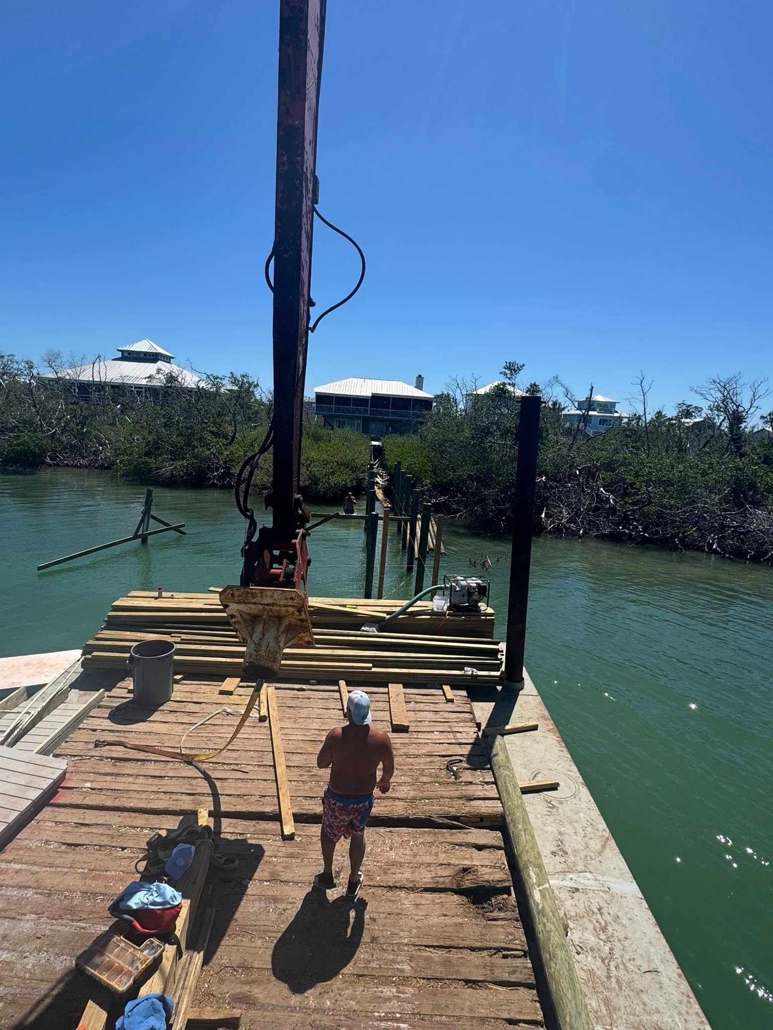 Wooden dock over turquoise water with stacked planks and a child walking toward the end under a bright blue sky
