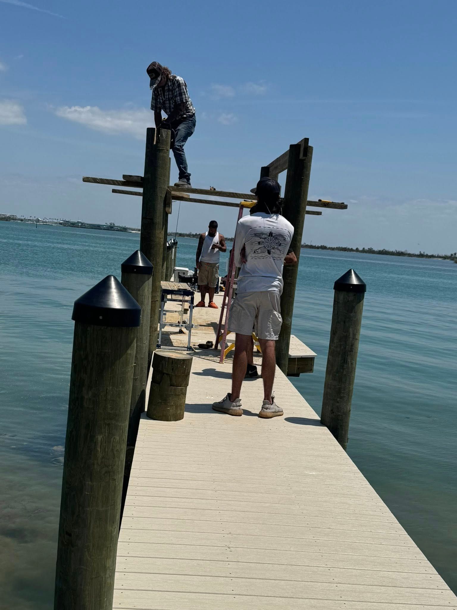 People standing on a dock over calm blue water, with a small boat lift ahead.