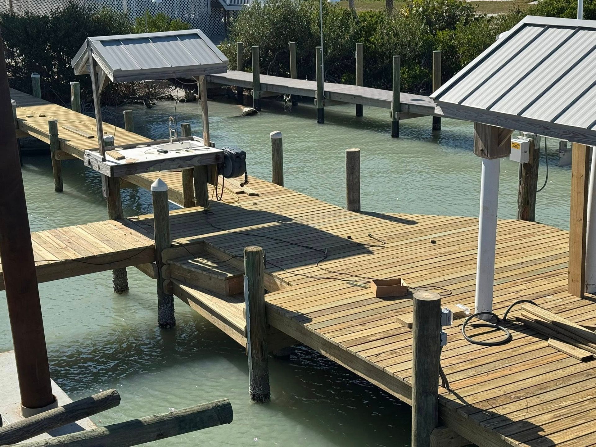 Wooden dock platforms over green water, with railings and small covered structures in bright sunlight.