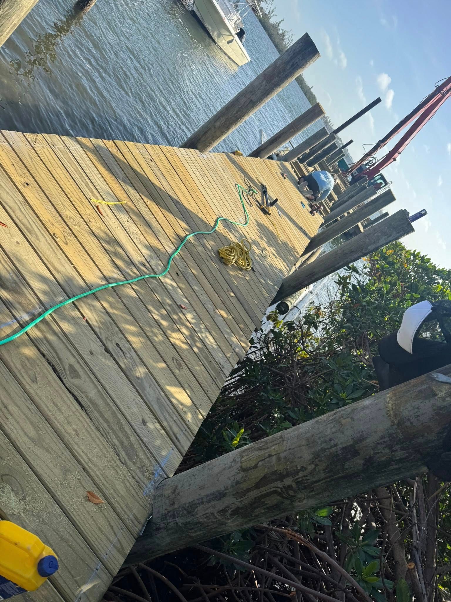 Wooden dock with green hose, bollards, and boats at a sunny waterfront