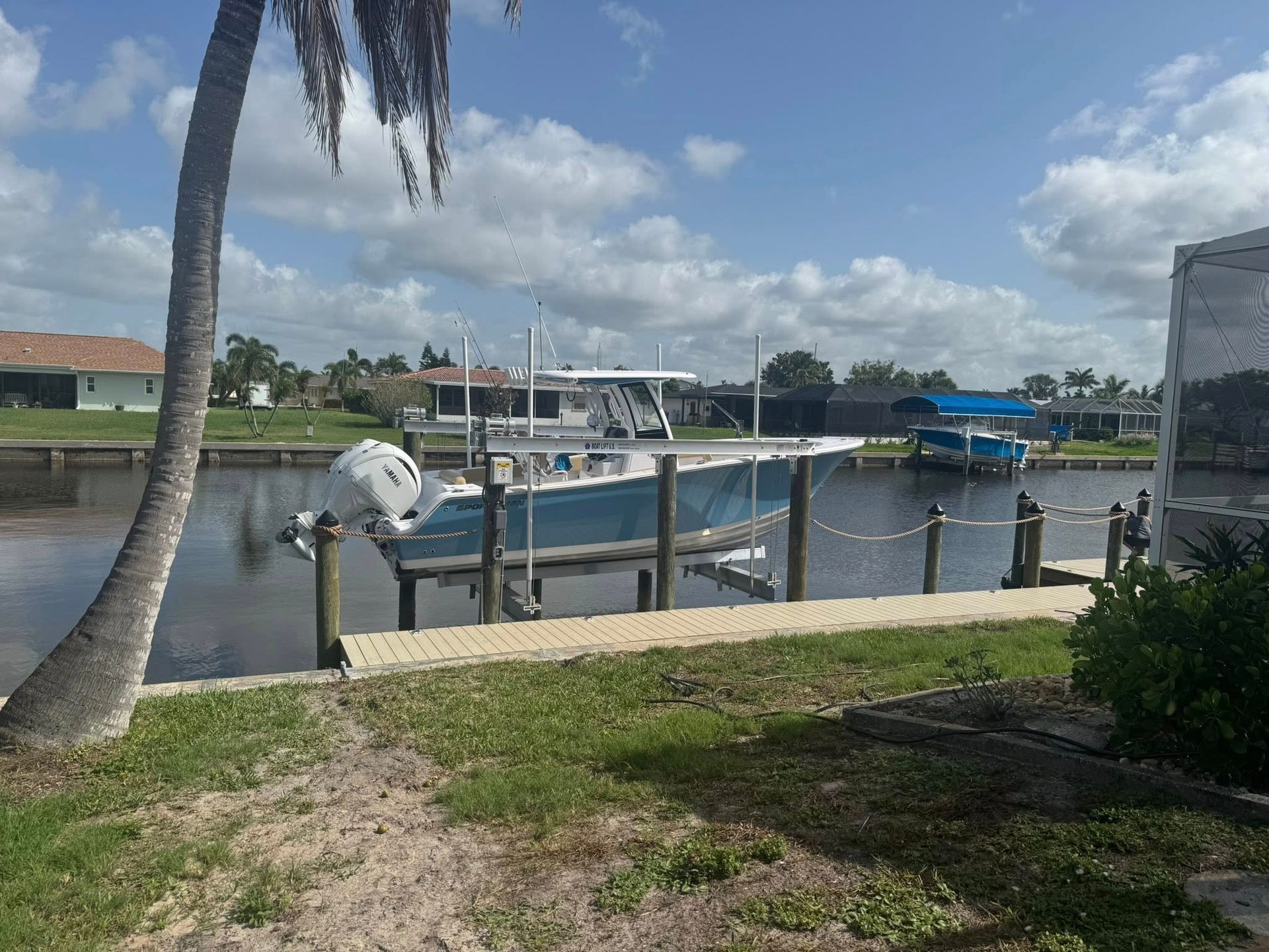 A white boat in a marina canal beside docks, with palm trees and a cloudy sky.