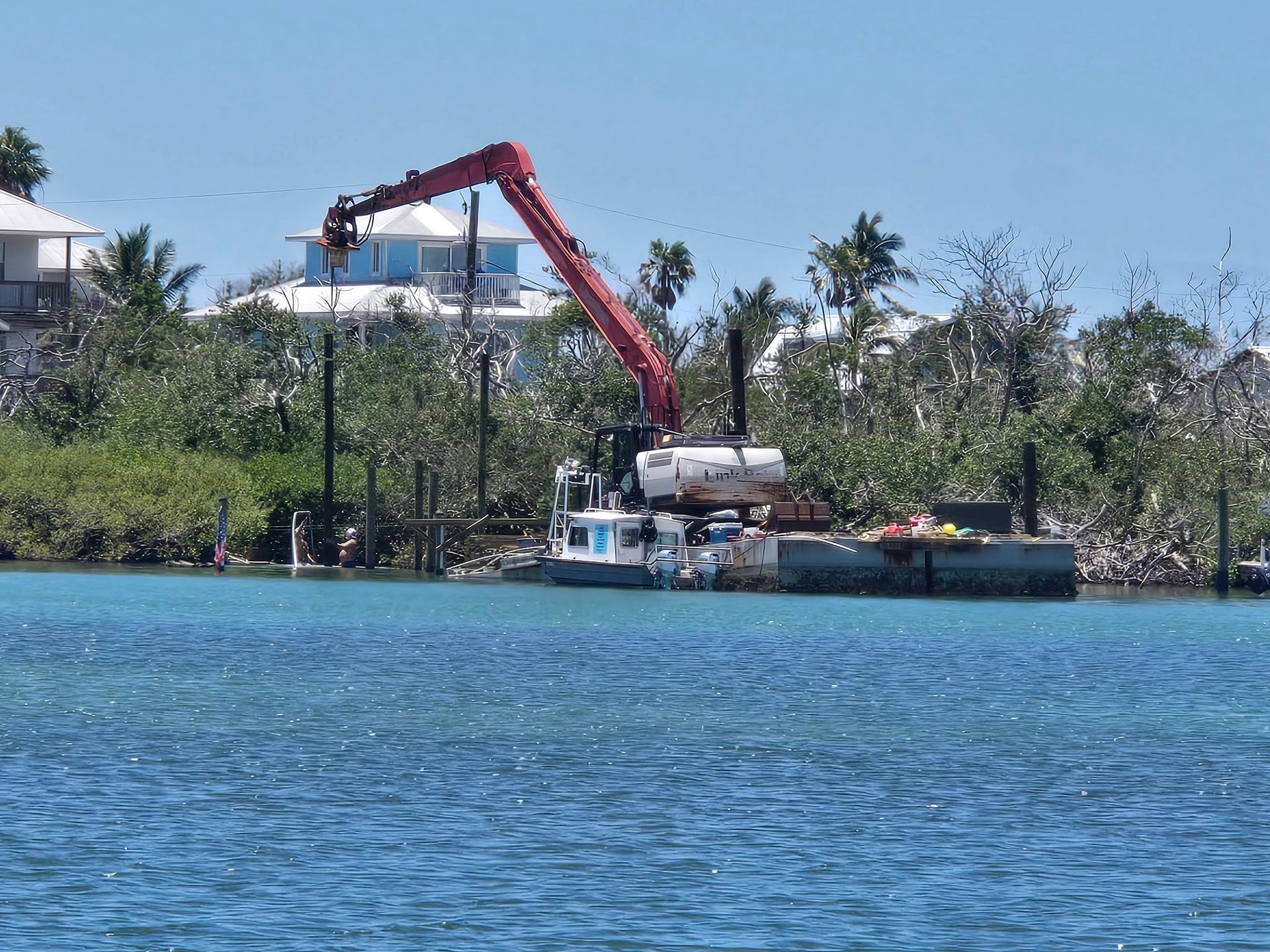 Red crane on a barge near a palm-lined shoreline over blue water