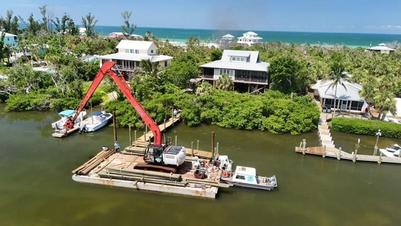 Red crane barge working in a tropical canal beside waterfront homes and lush greenery