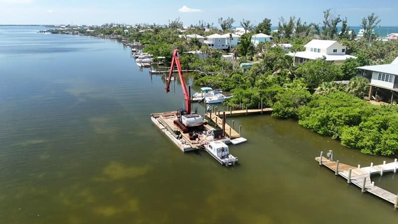 Aerial view of a red crane barge on a calm green river beside homes and docks.