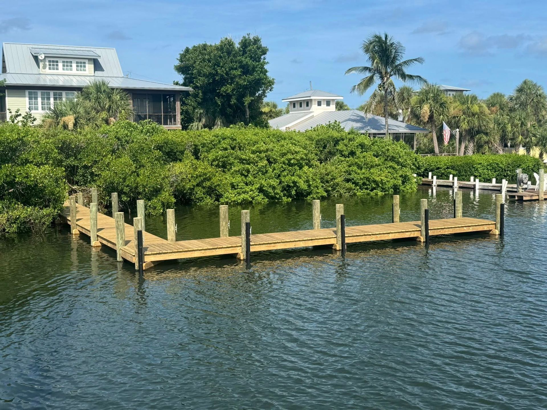 Dock around lush green island in calm water with houses and palm trees in the background