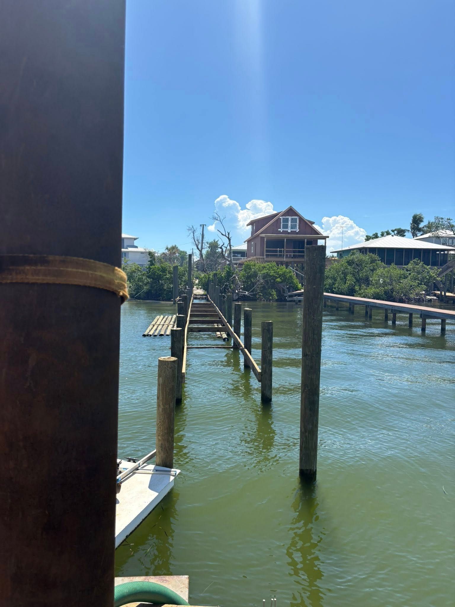 Docks and pilings on a sunny waterfront, with a small building over the water and clear blue sky.