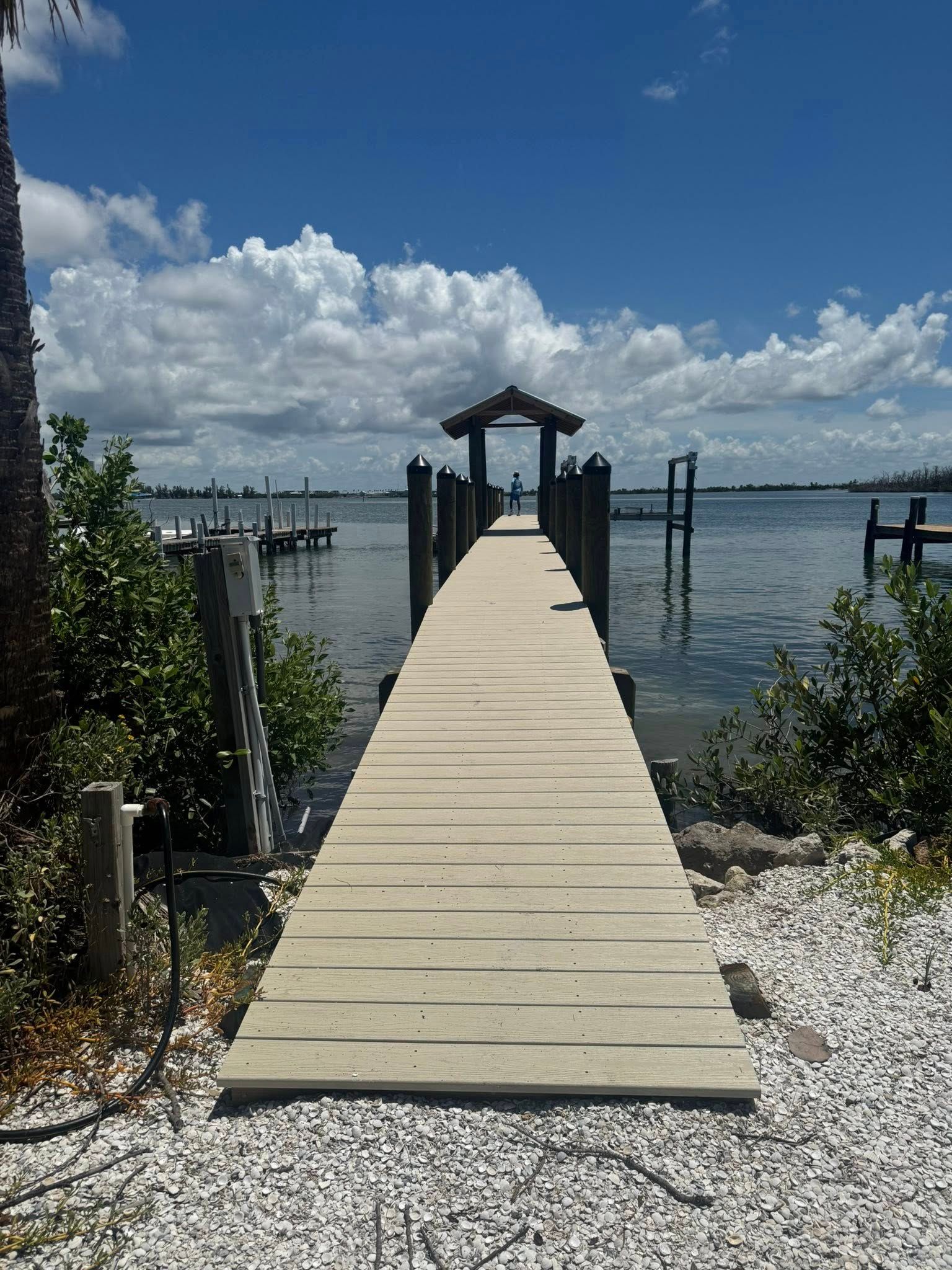 Wooden dock leading to a small gazebo over calm water under a bright, cloudy sky