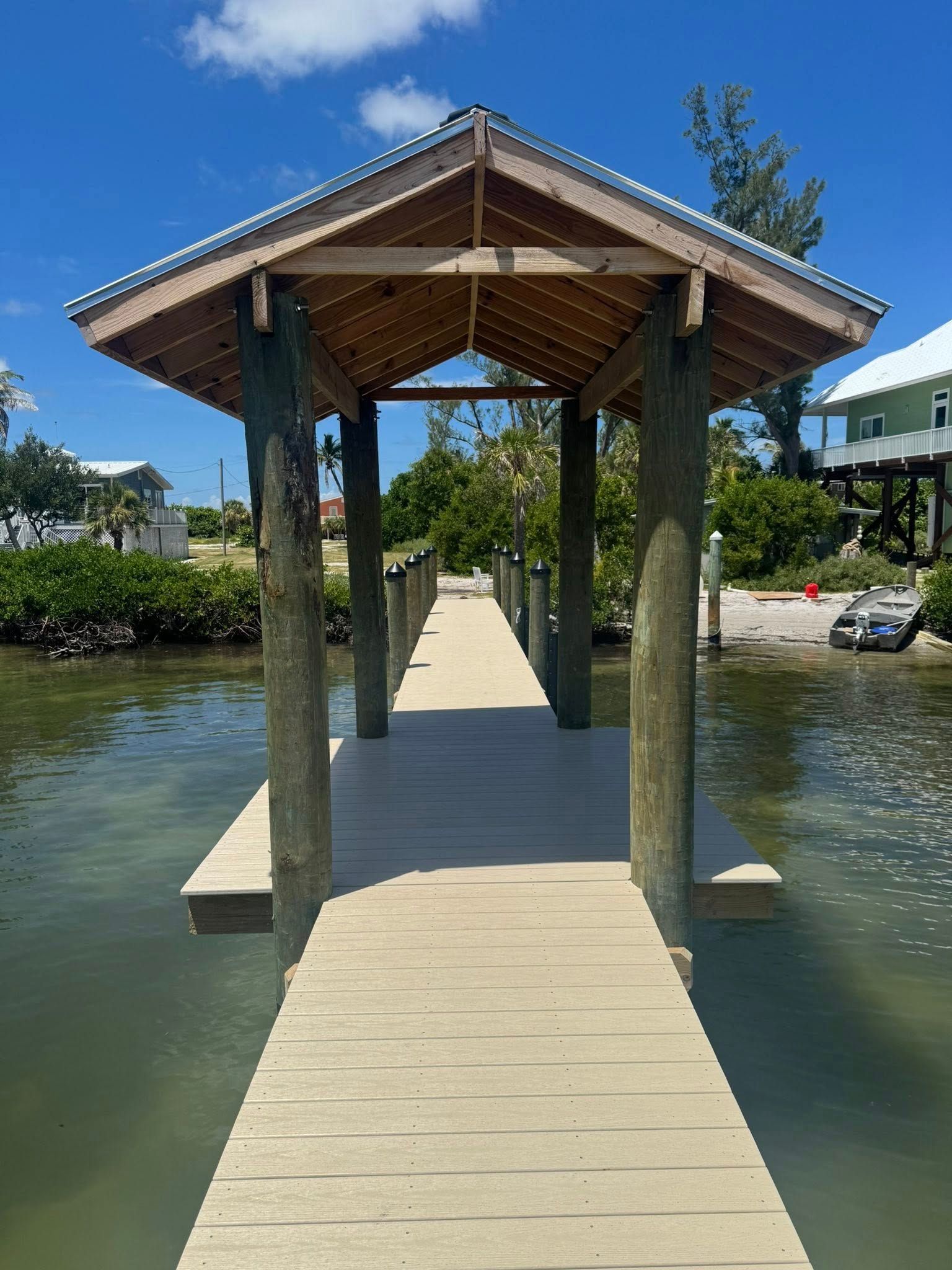 Wooden walkway and gazebo over calm water under a sunny blue sky.