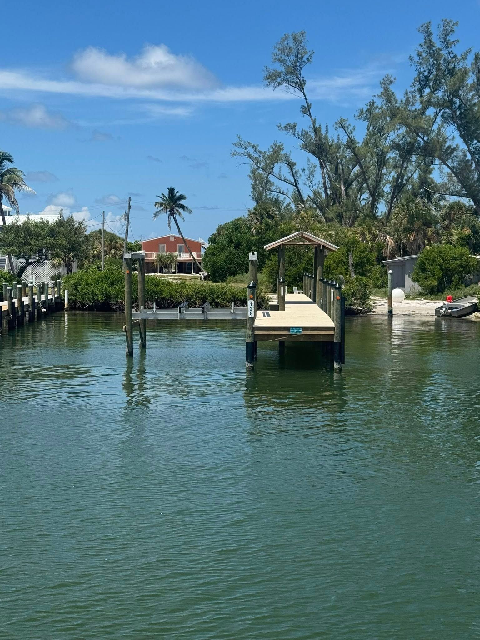 Canal with a small dock, tropical trees, and houses under a sunny blue sky