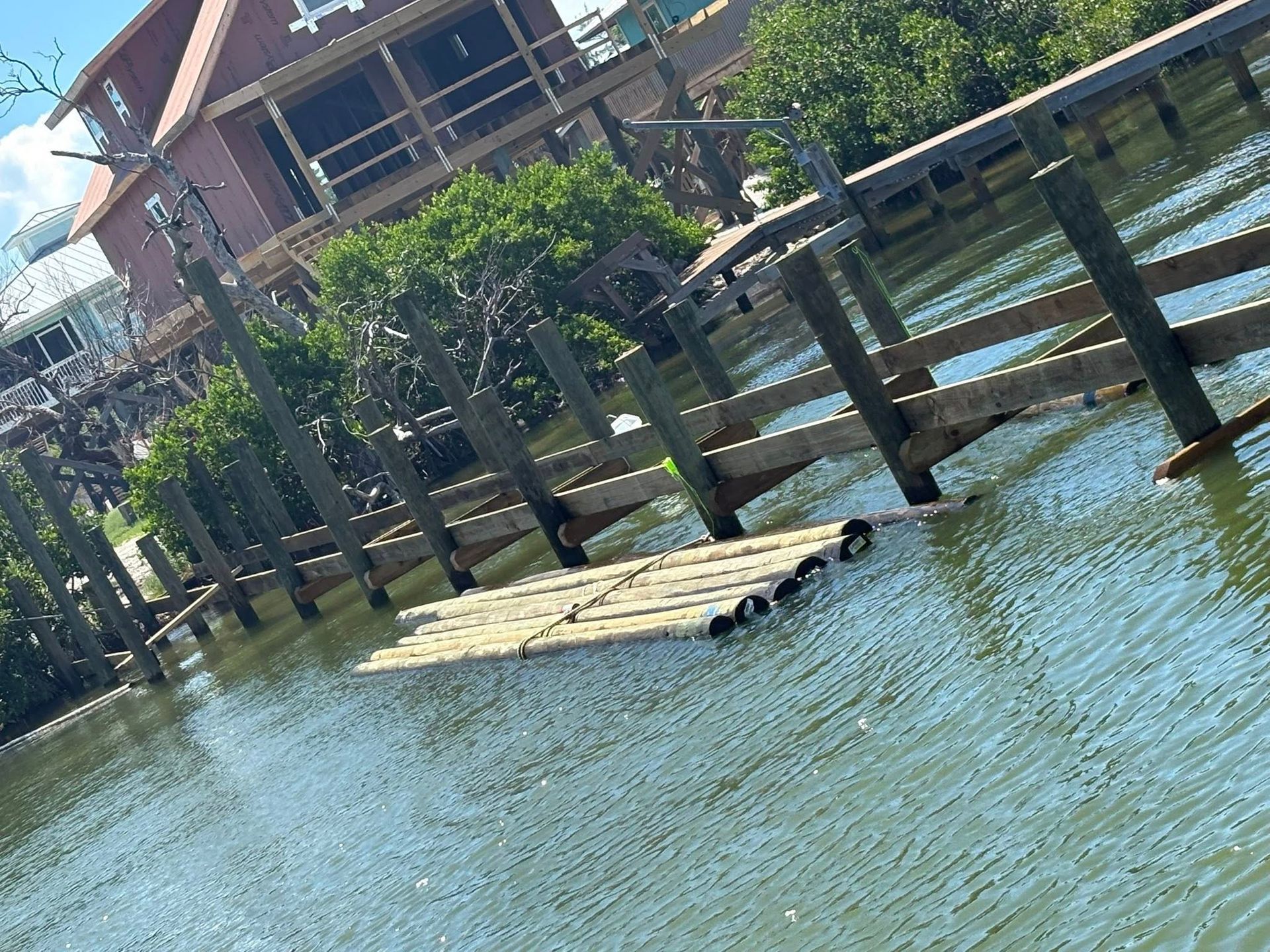 Floating bamboo raft on calm blue water beside a wooden riverside deck and tree-covered building.