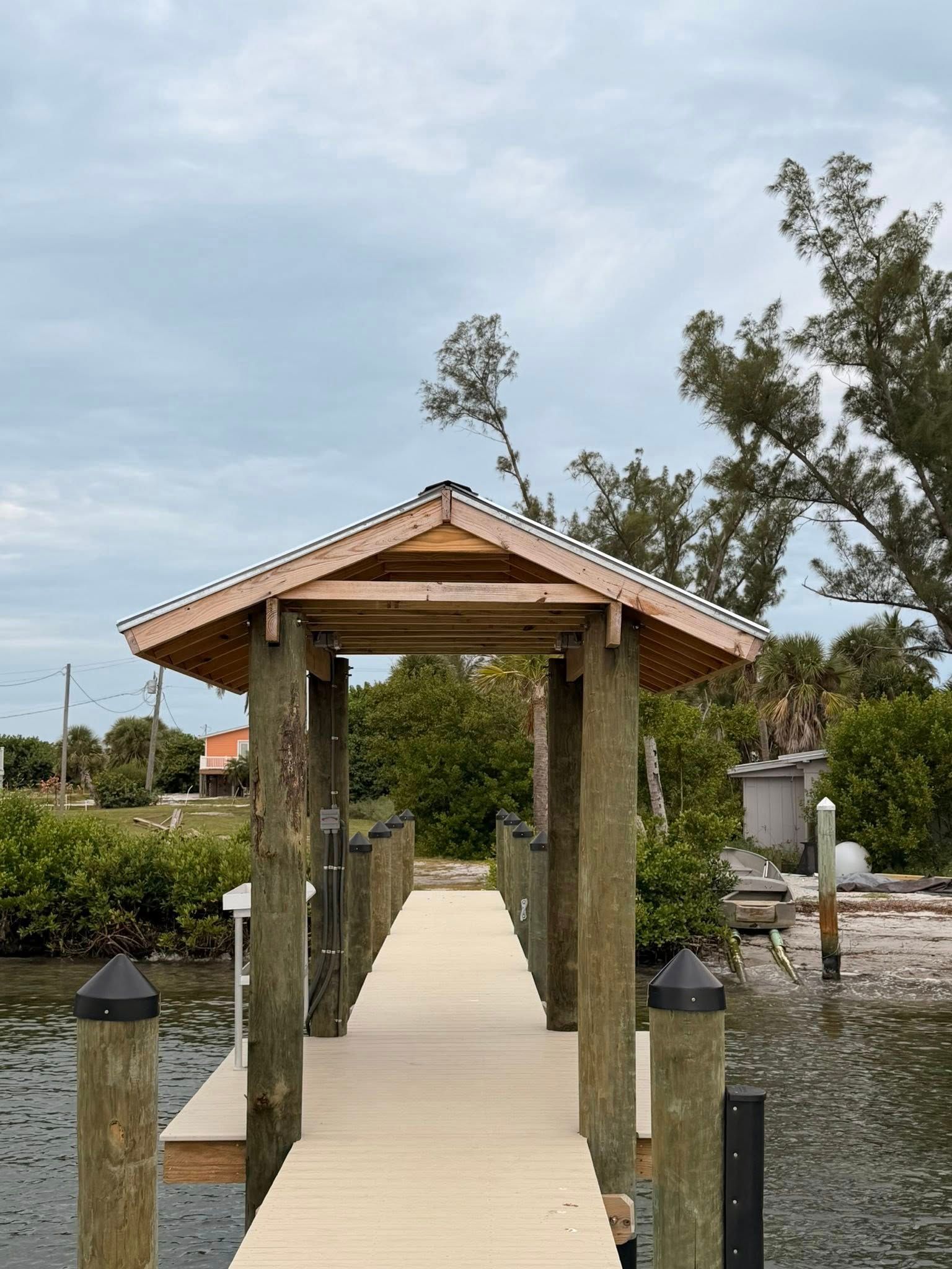 Wooden walkway leading to a small thatched gazebo over water in a landscaped garden