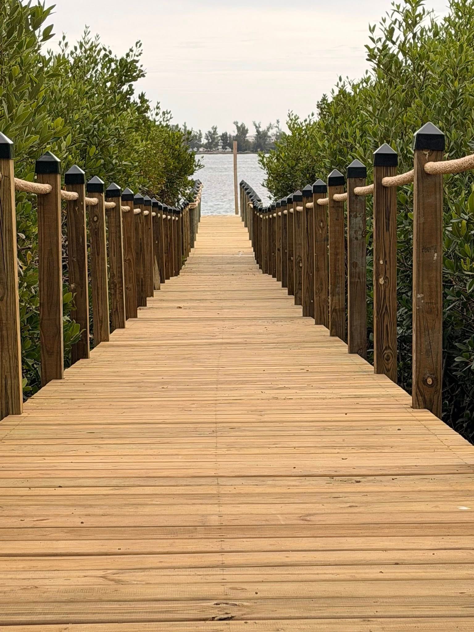 Wooden boardwalk leading through greenery to a calm waterfront under a hazy sky