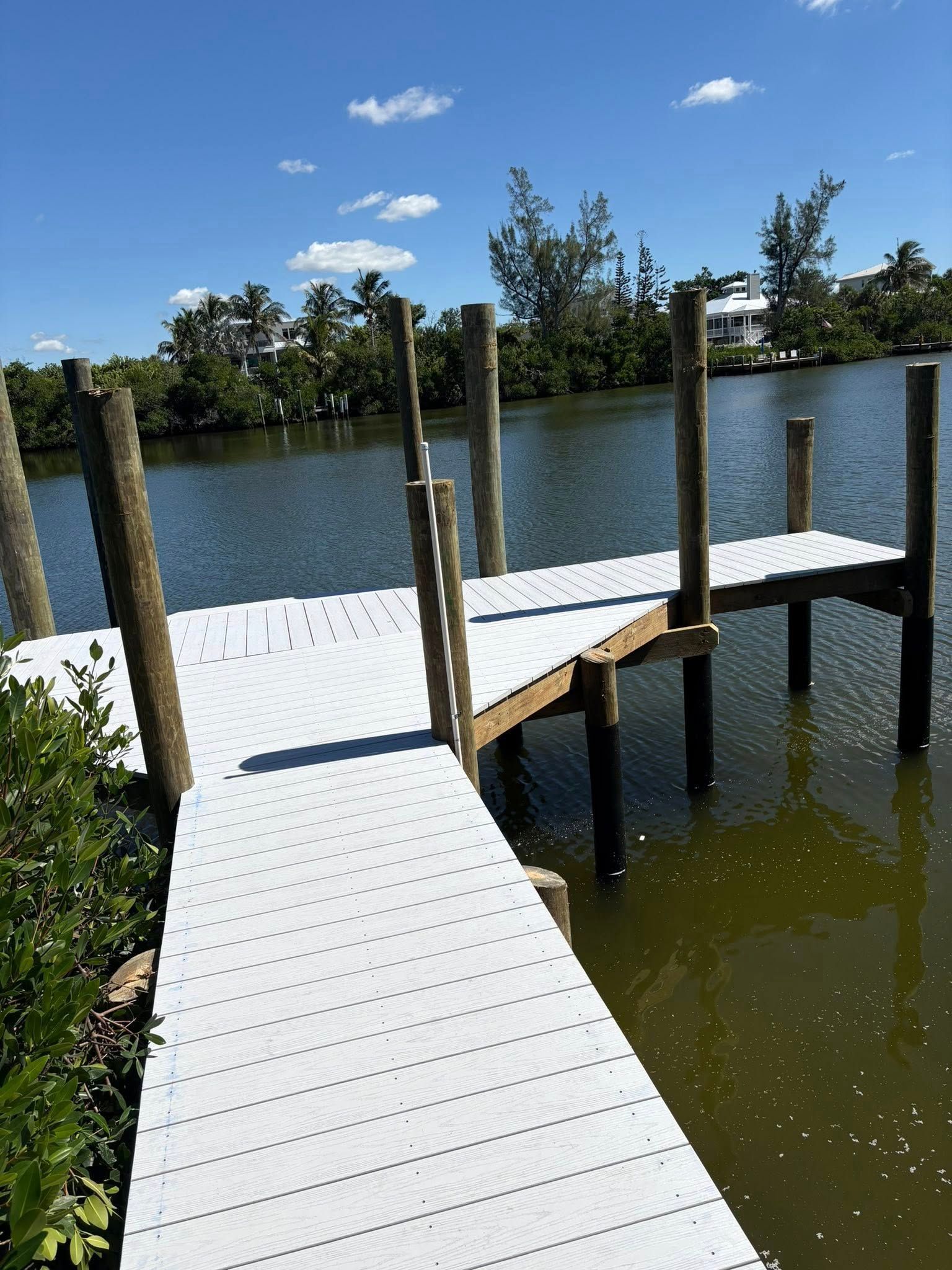 White dock extending into a calm lake under a blue sky with scattered clouds