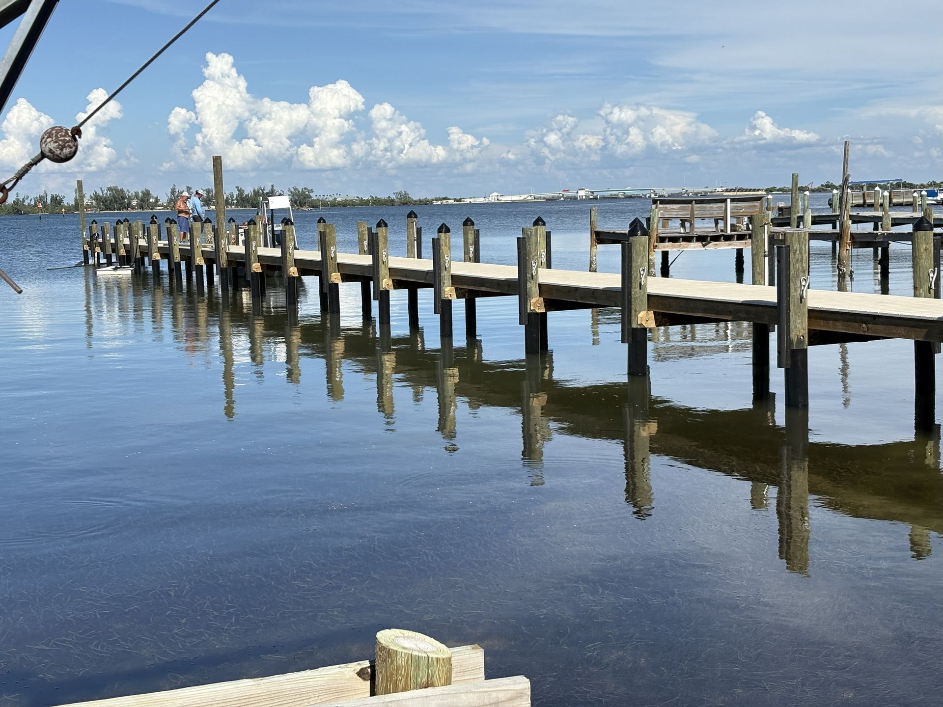 Calm marina with wooden dock and pilings reflected in still blue water under a clear sky