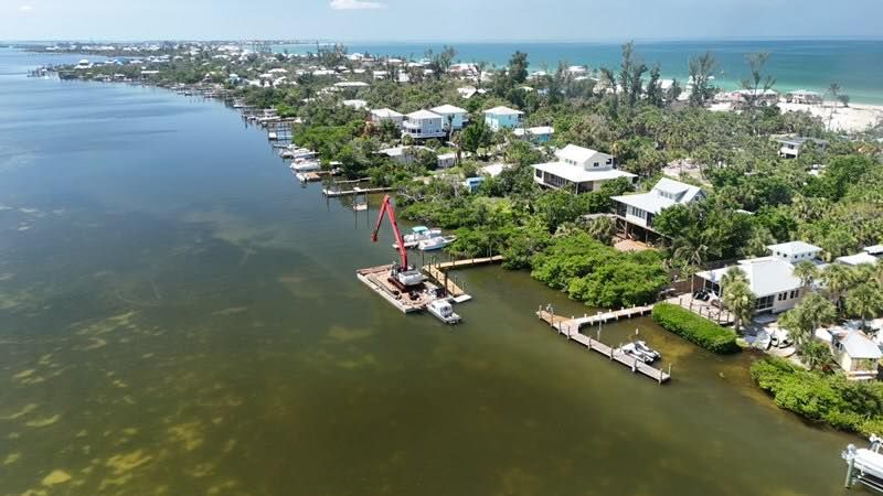 Aerial view of a waterfront neighborhood with docks, boats, and green shoreline along calm water.
