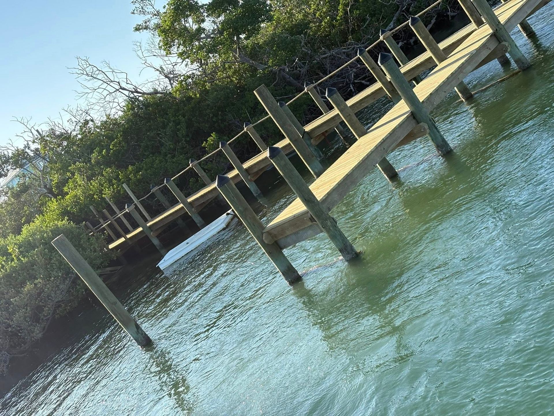 Wooden dock extending over calm blue-green water beside dense trees and a sandy shore