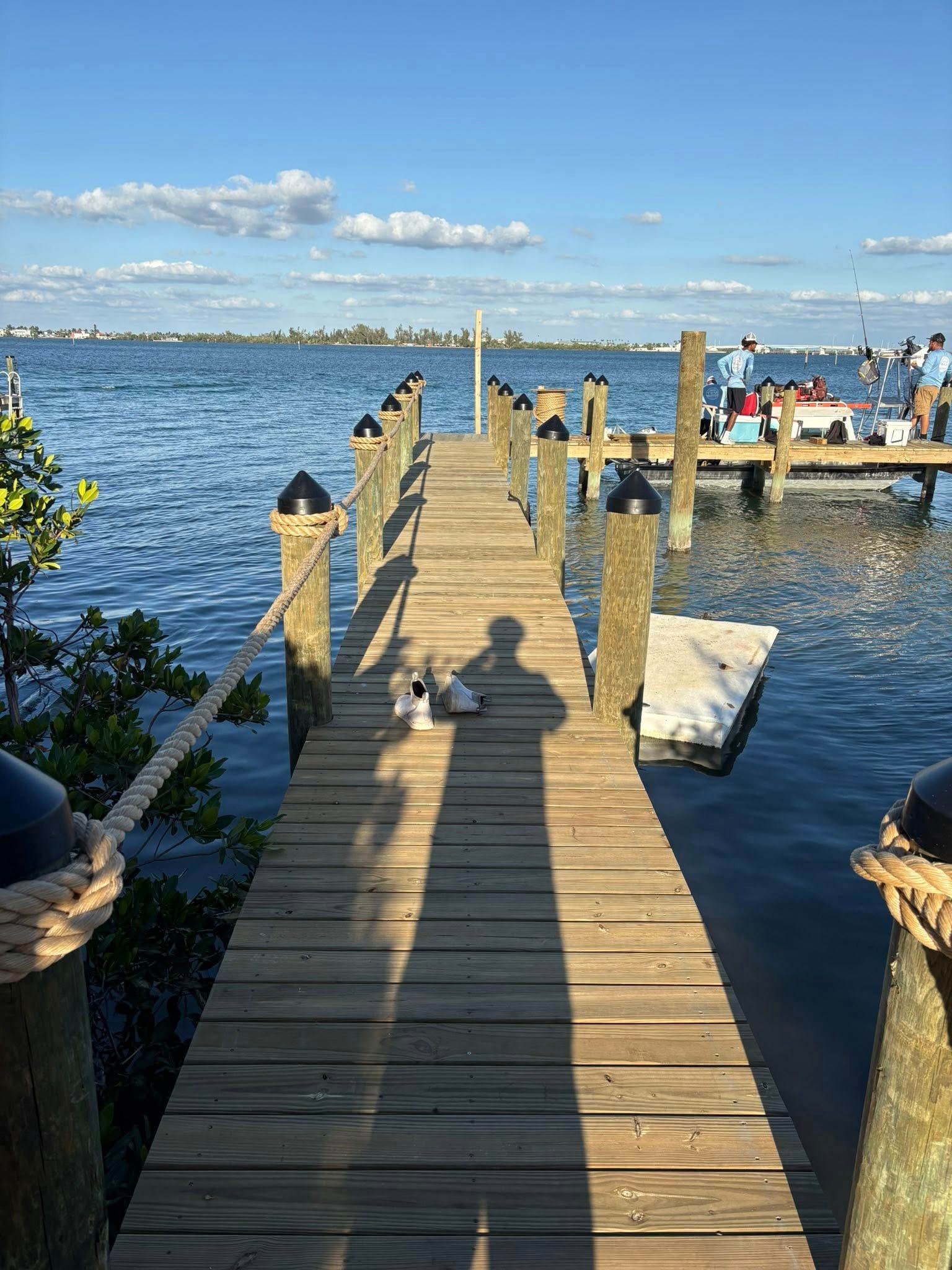 Wooden dock over blue water leading to a distant lakeside pier under a bright sky