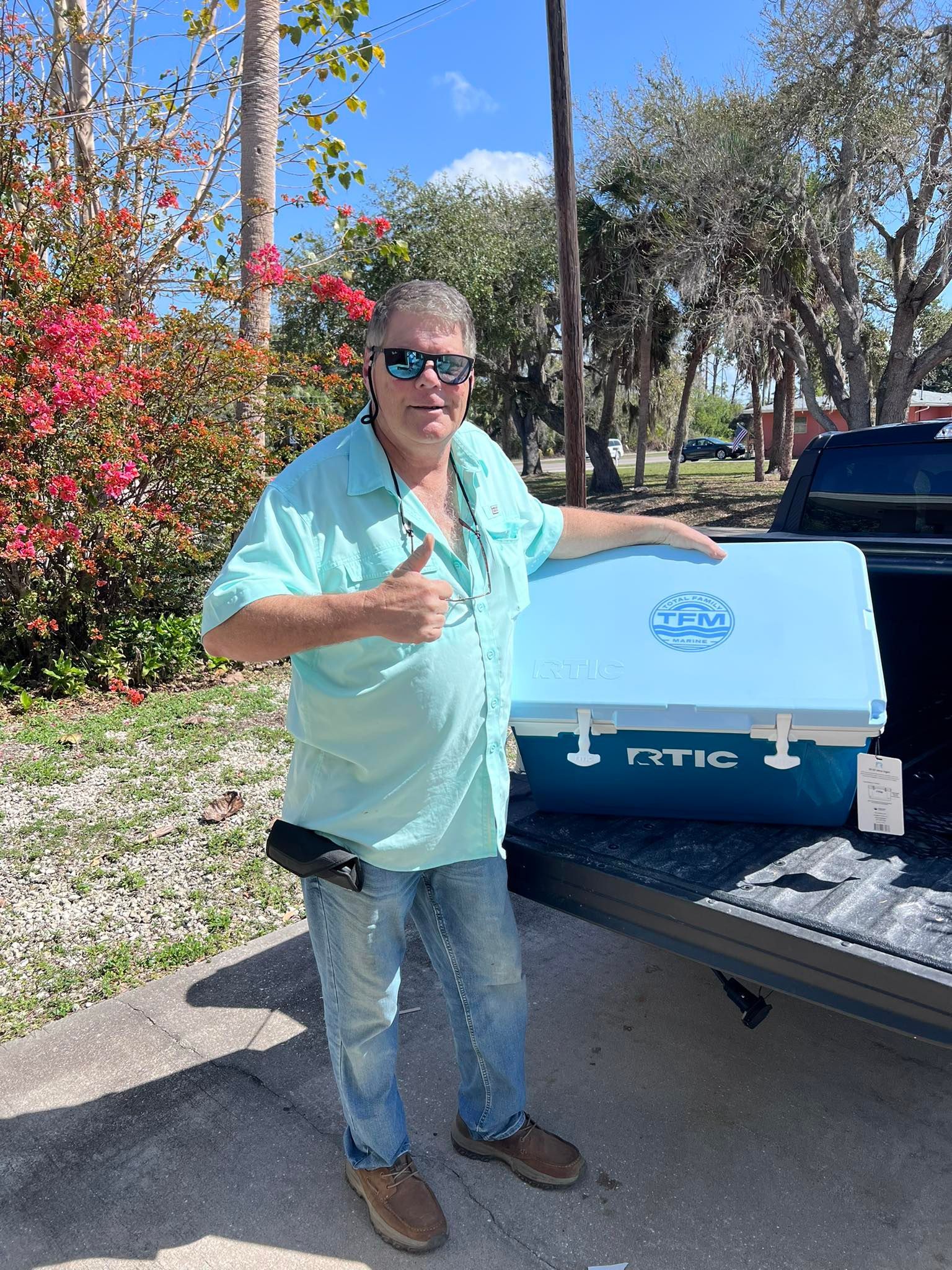 Man standing beside a blue YETI cooler in the back of a truck, outdoors in sunlight.
