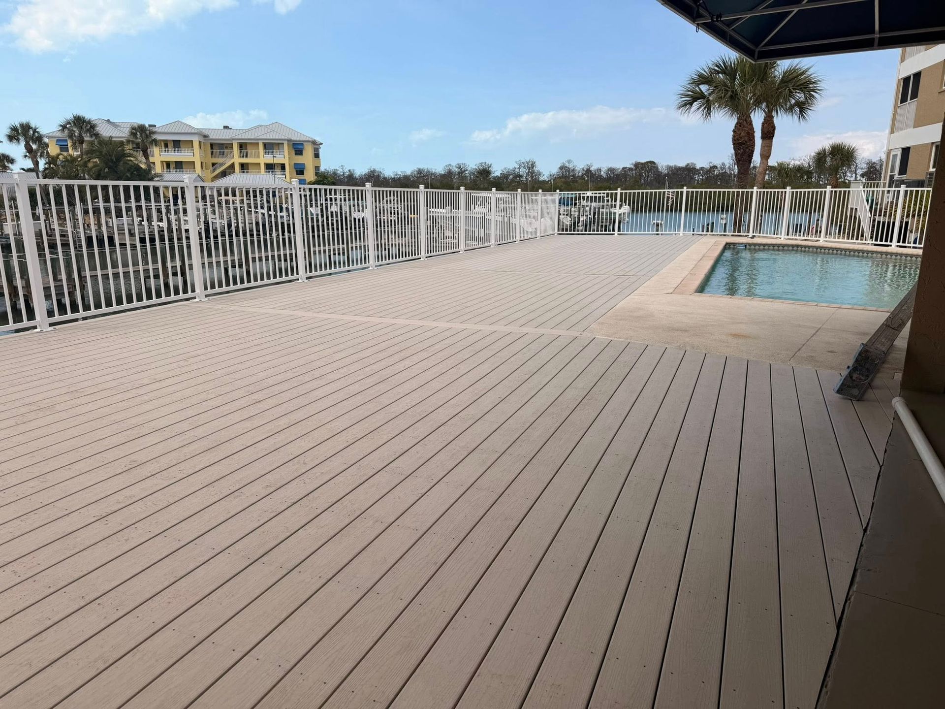 Poolside deck with white railing and beige flooring beside a blue swimming pool under a canopy