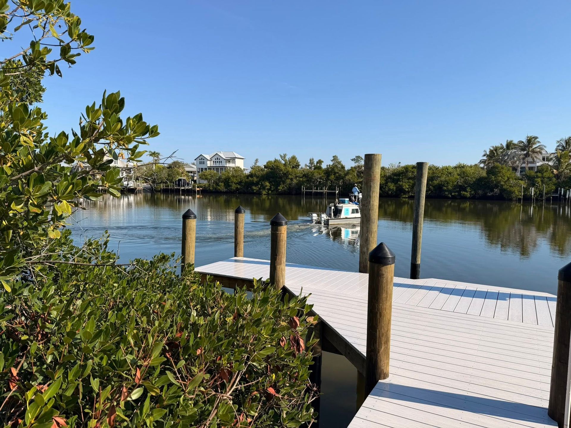 White dock on calm lake with boats and trees under a clear blue sky