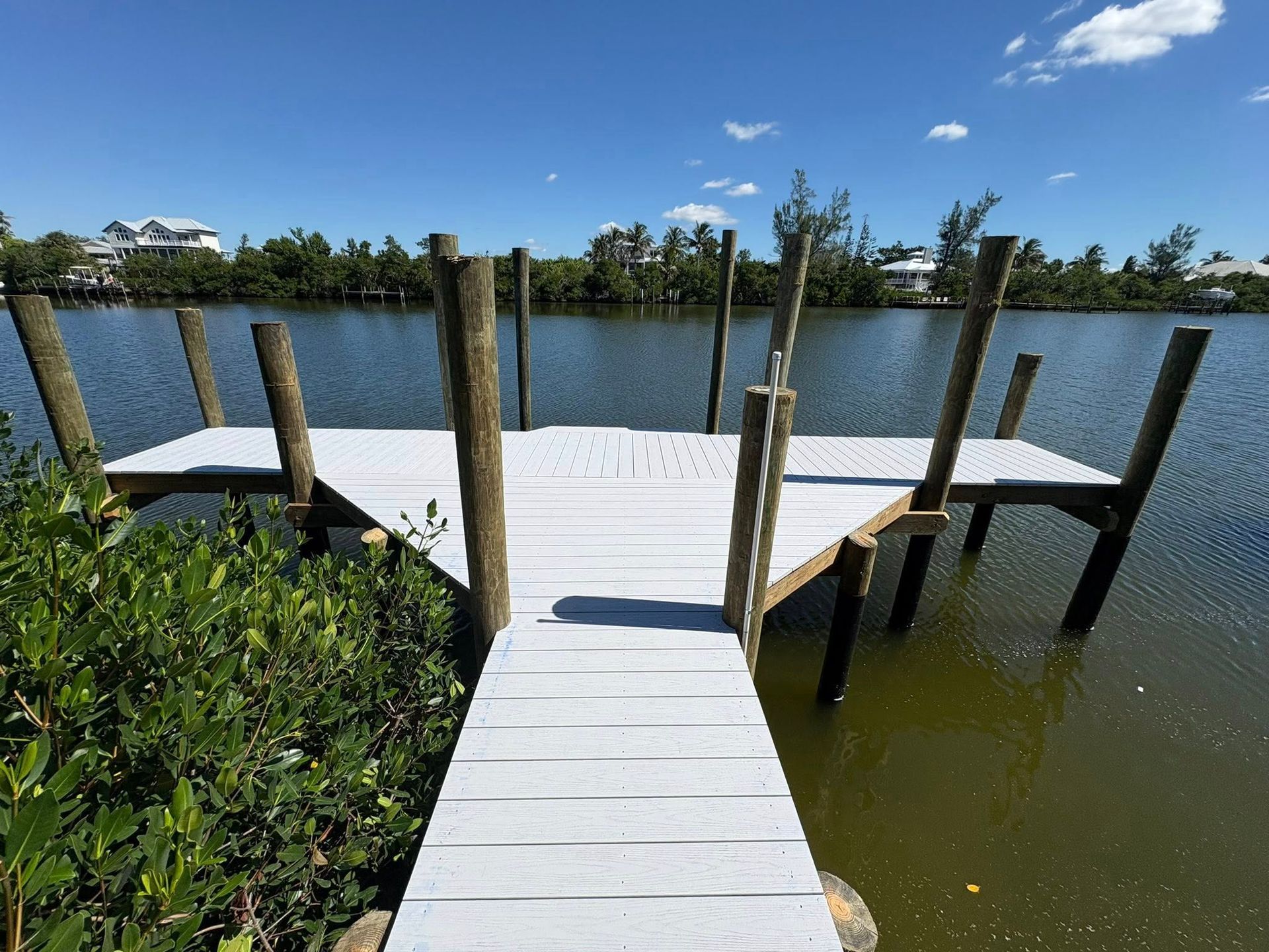 Wooden dock with white boards extending into a calm lake under a blue sky