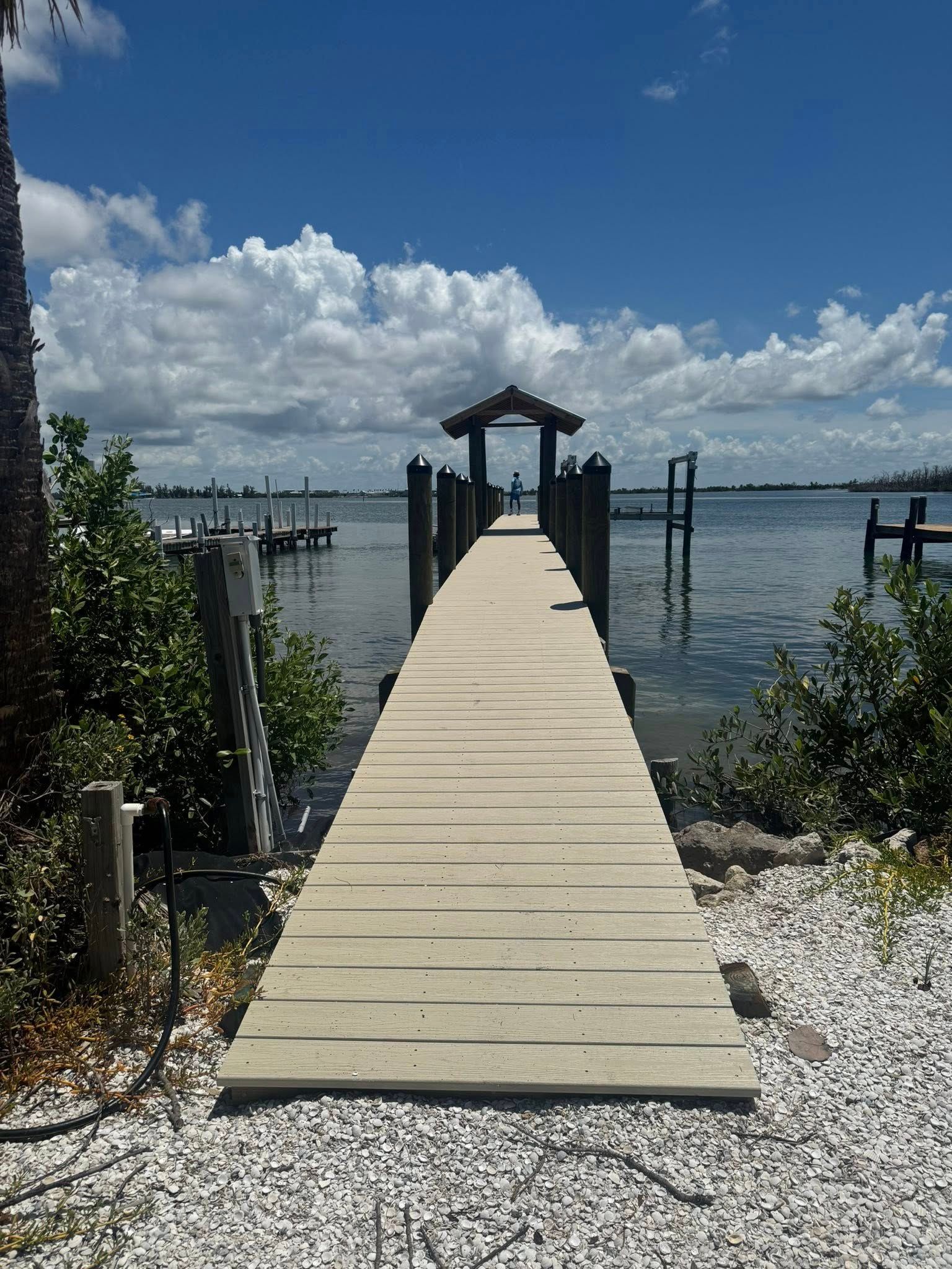 Wooden dock leading to a covered pier over calm water under a partly cloudy blue sky
