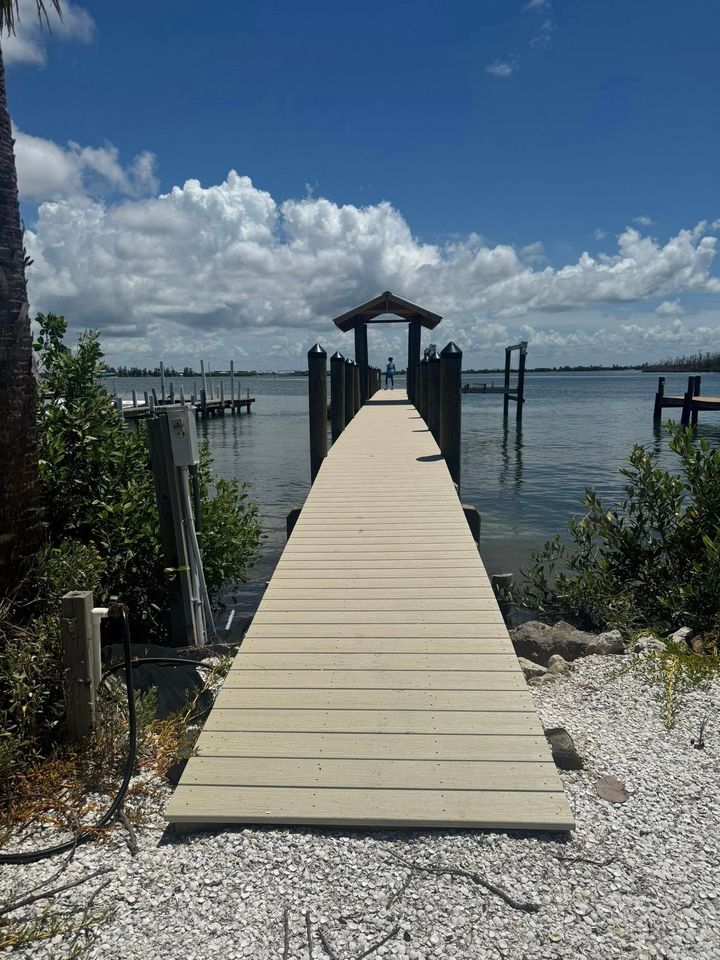 Wooden dock leading to a covered pier over calm water under a partly cloudy blue sky