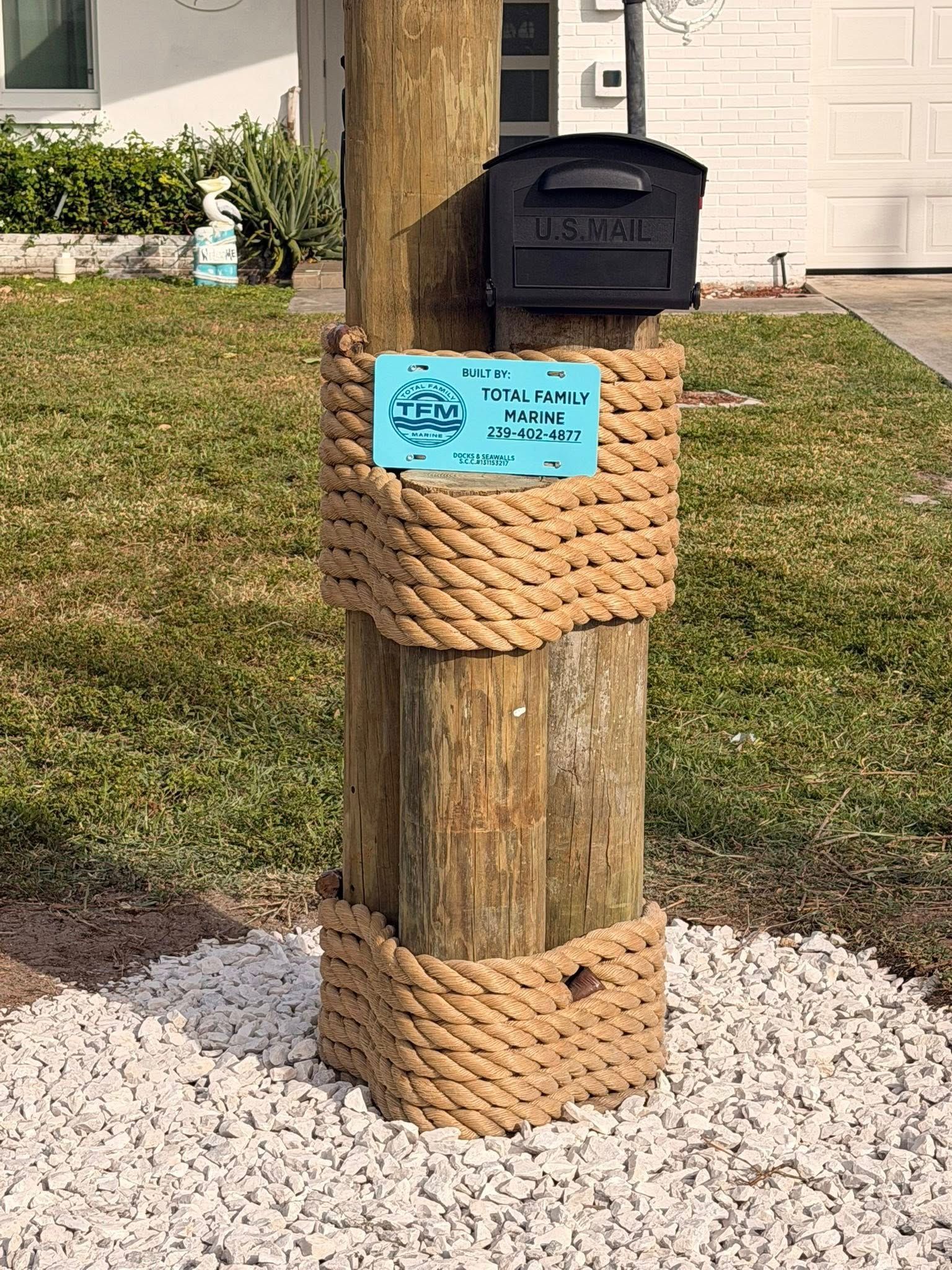 Wooden post with black mailbox wrapped in rope, standing in a landscaped yard with white gravel.