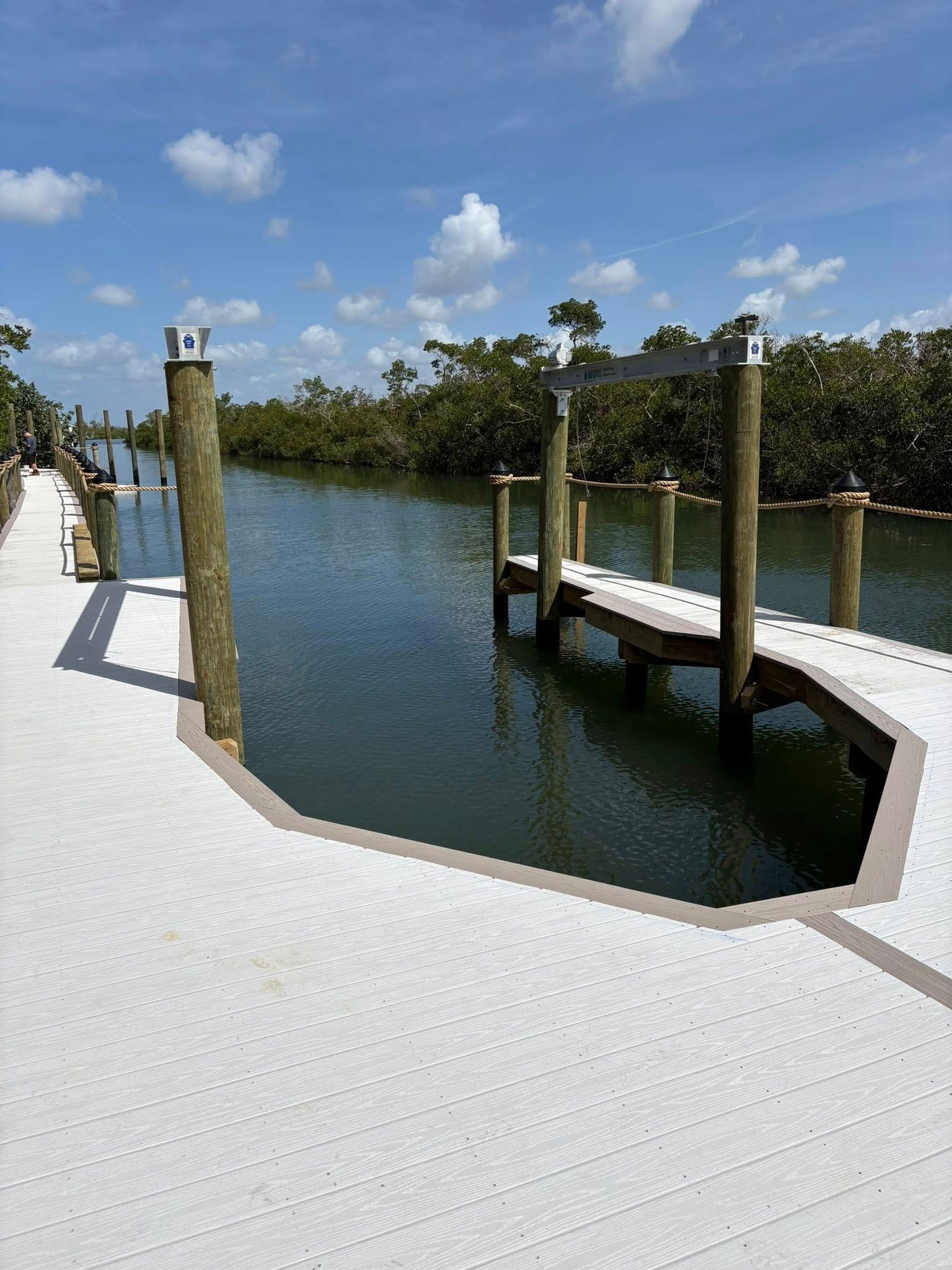 White waterfront deck with dock, calm water, and palm trees under a blue sky