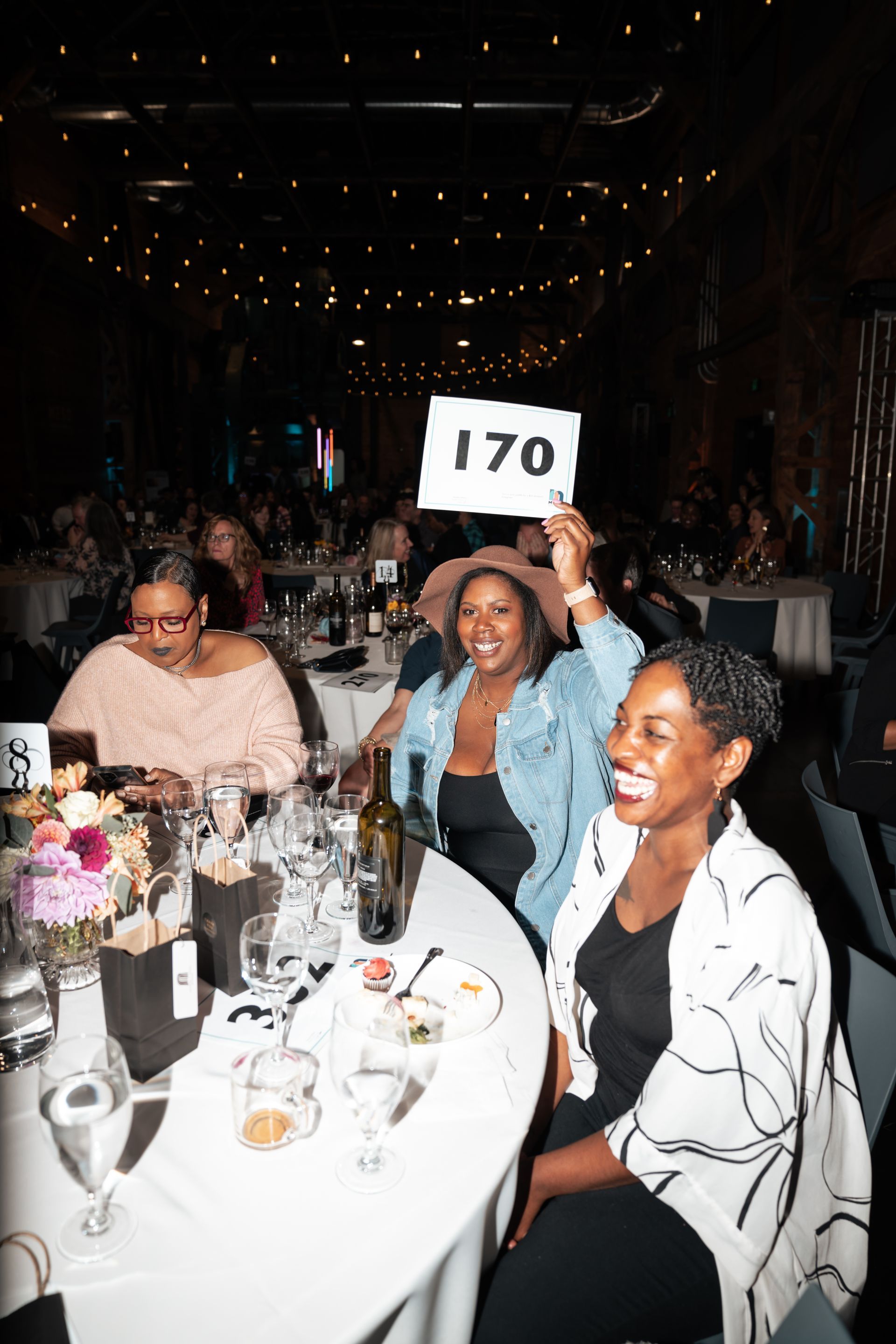 A woman is sitting at a table holding a sign that says 170.