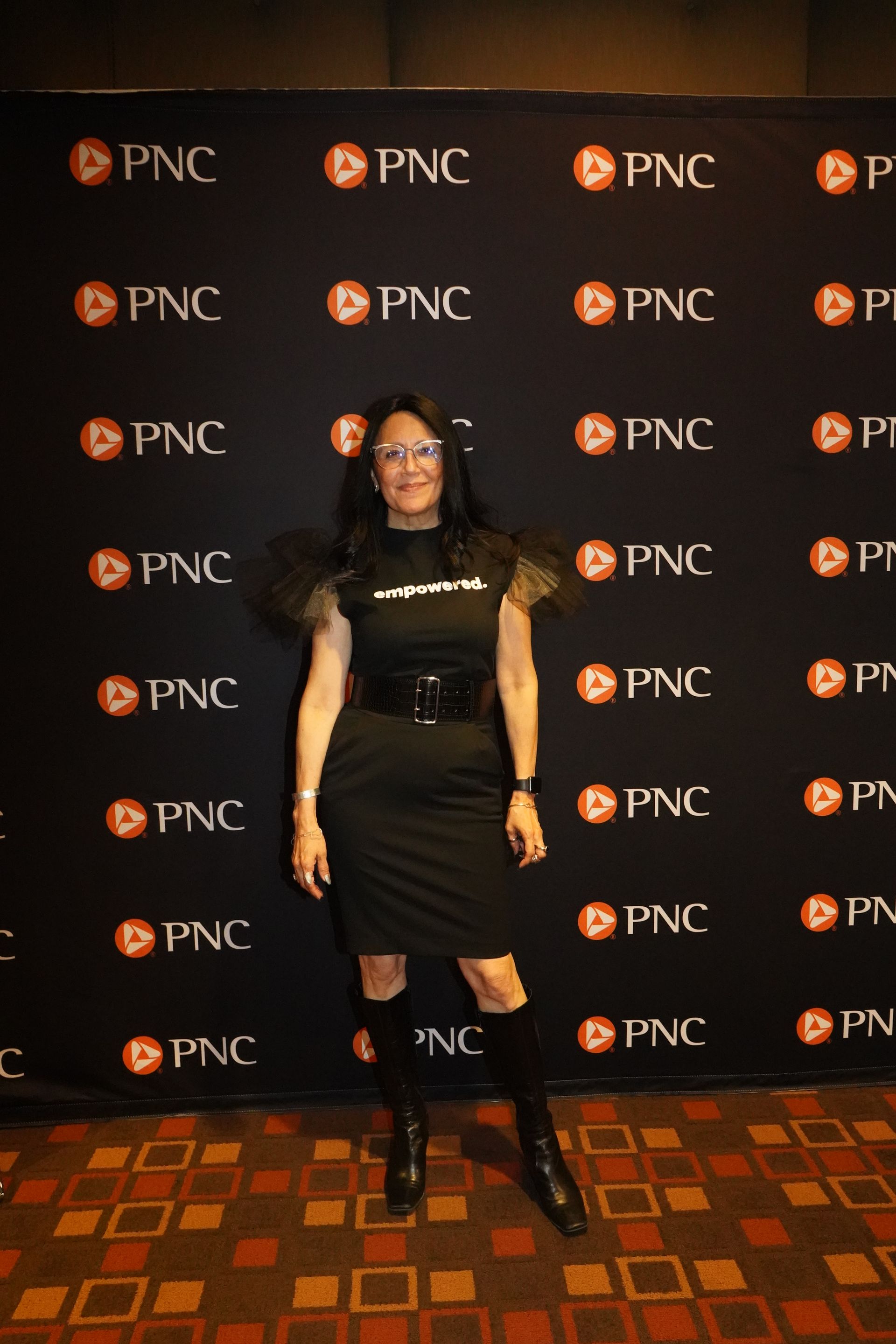 A woman in a black dress is standing in front of a pnc backdrop