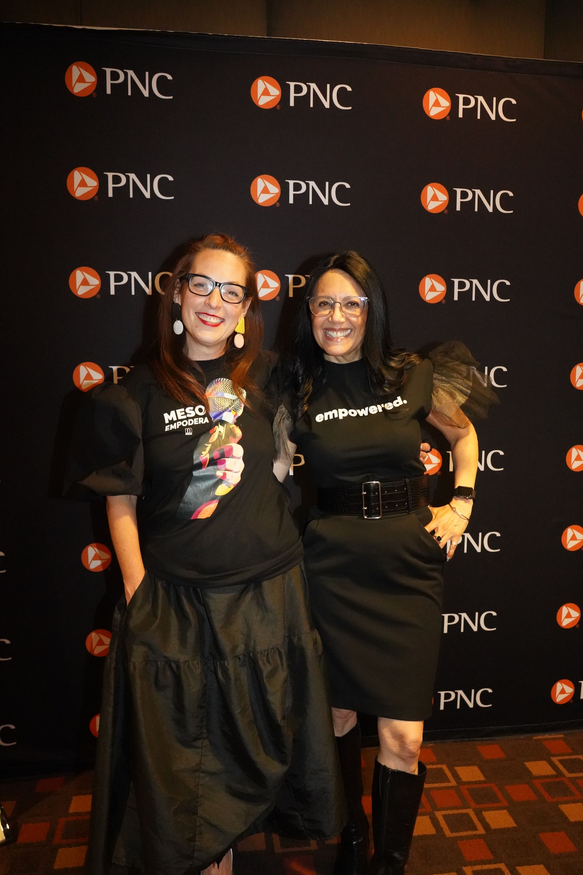 Two women are posing for a picture in front of a pnc backdrop