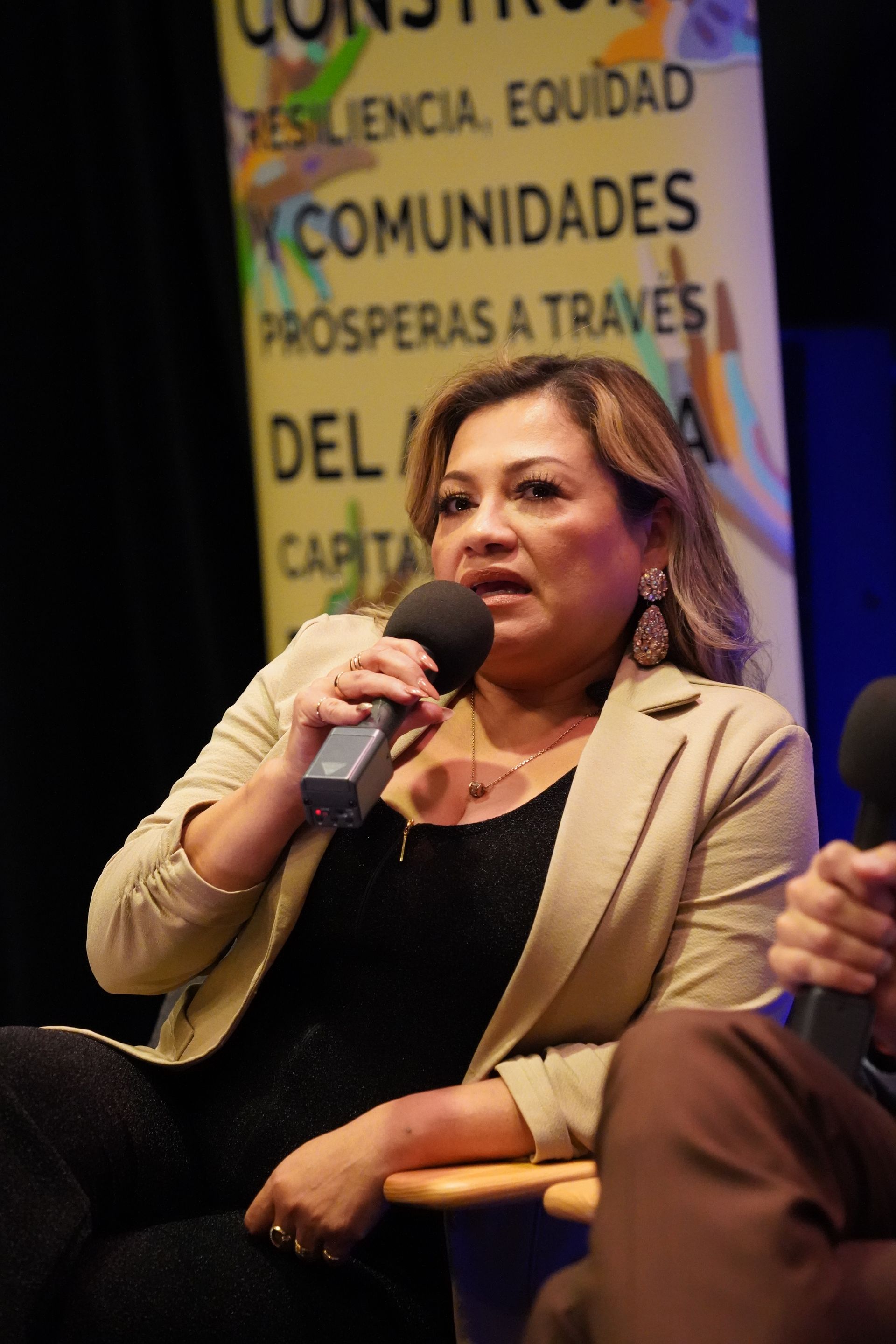 A woman is holding a microphone in front of a sign that says comunidades