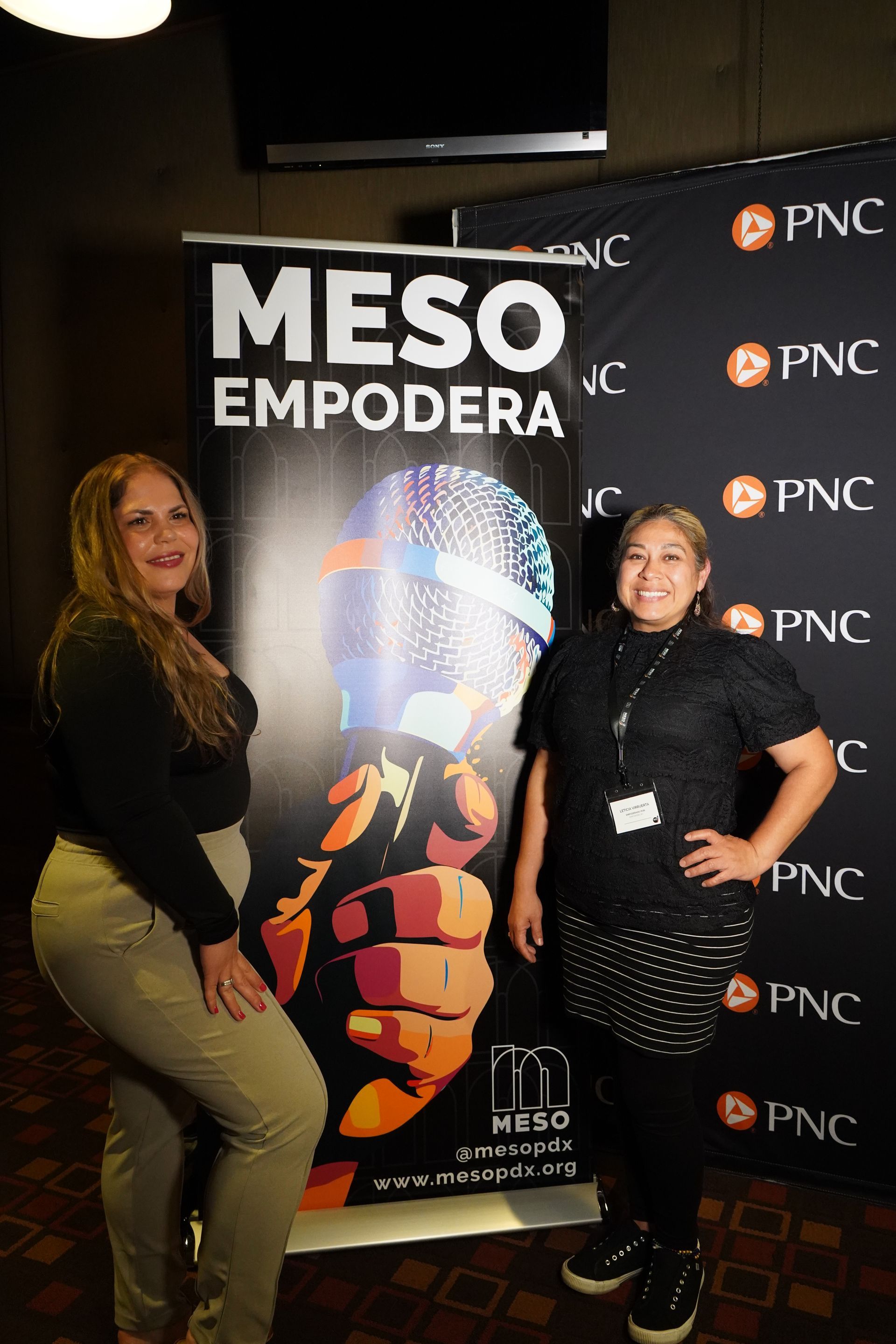 Two women are standing next to each other in front of a banner that says meso empodera.