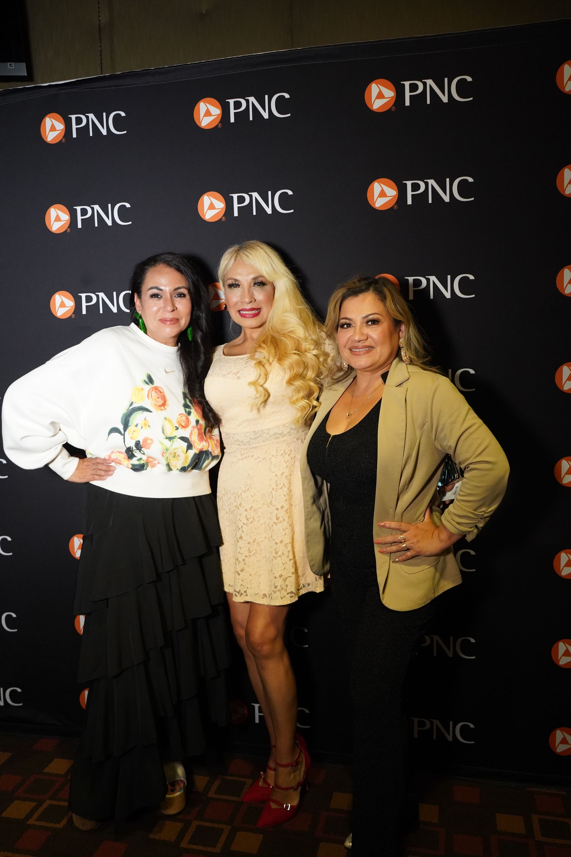 Three women are posing for a picture in front of a pnc backdrop.