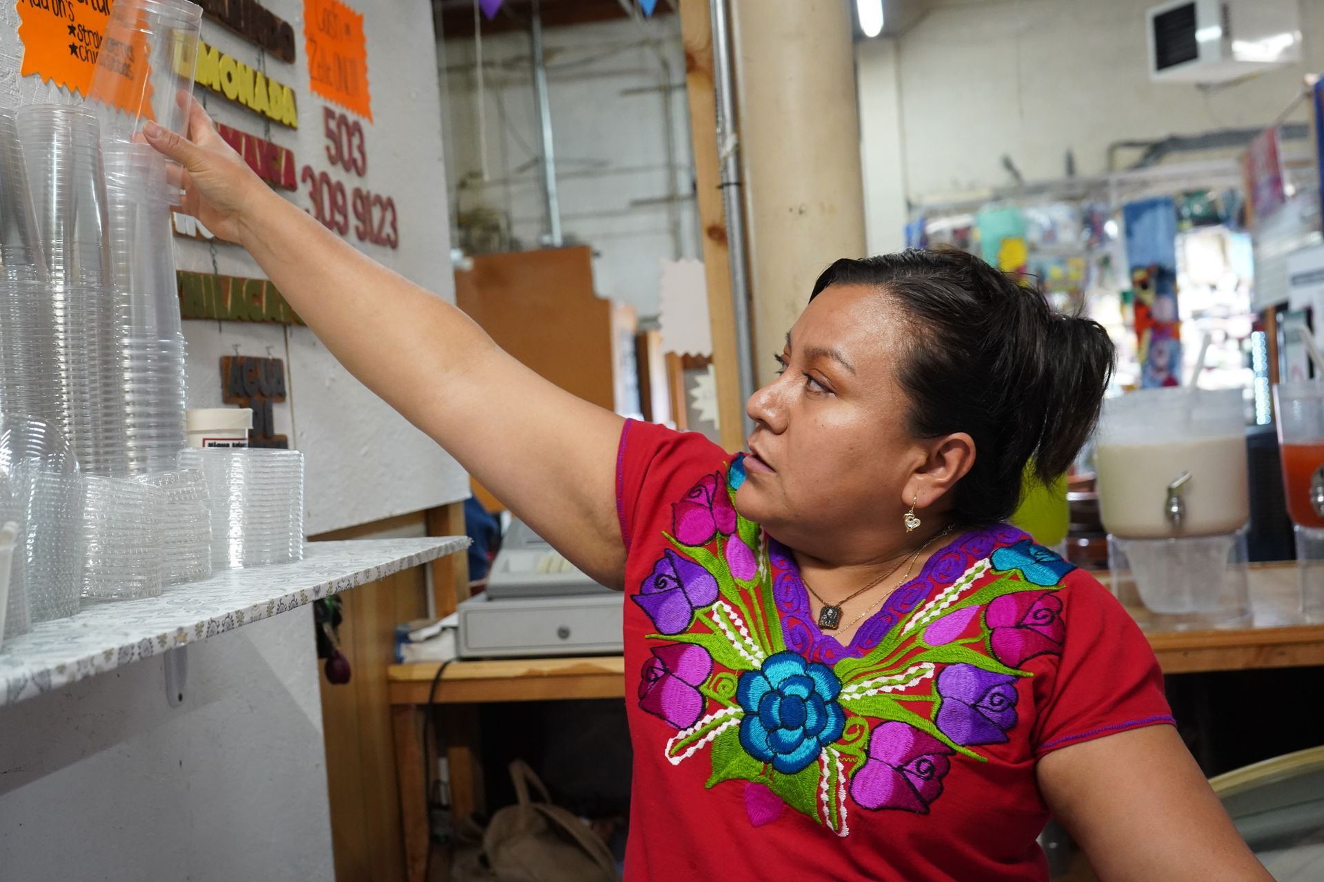 A woman in a red shirt is reaching for a cup in a store.