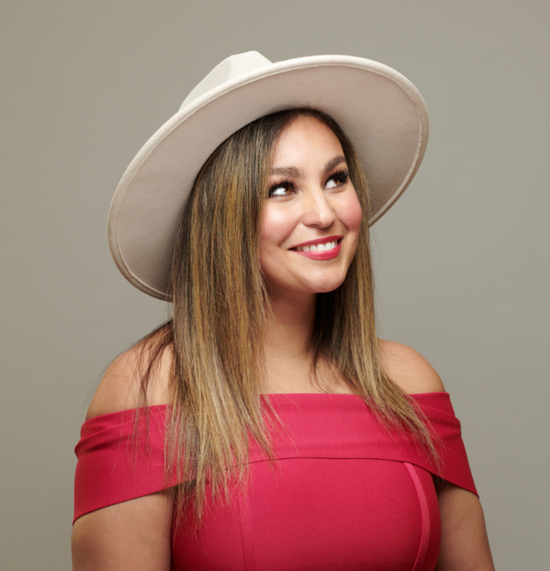 A woman wearing a red dress and a white hat is smiling.