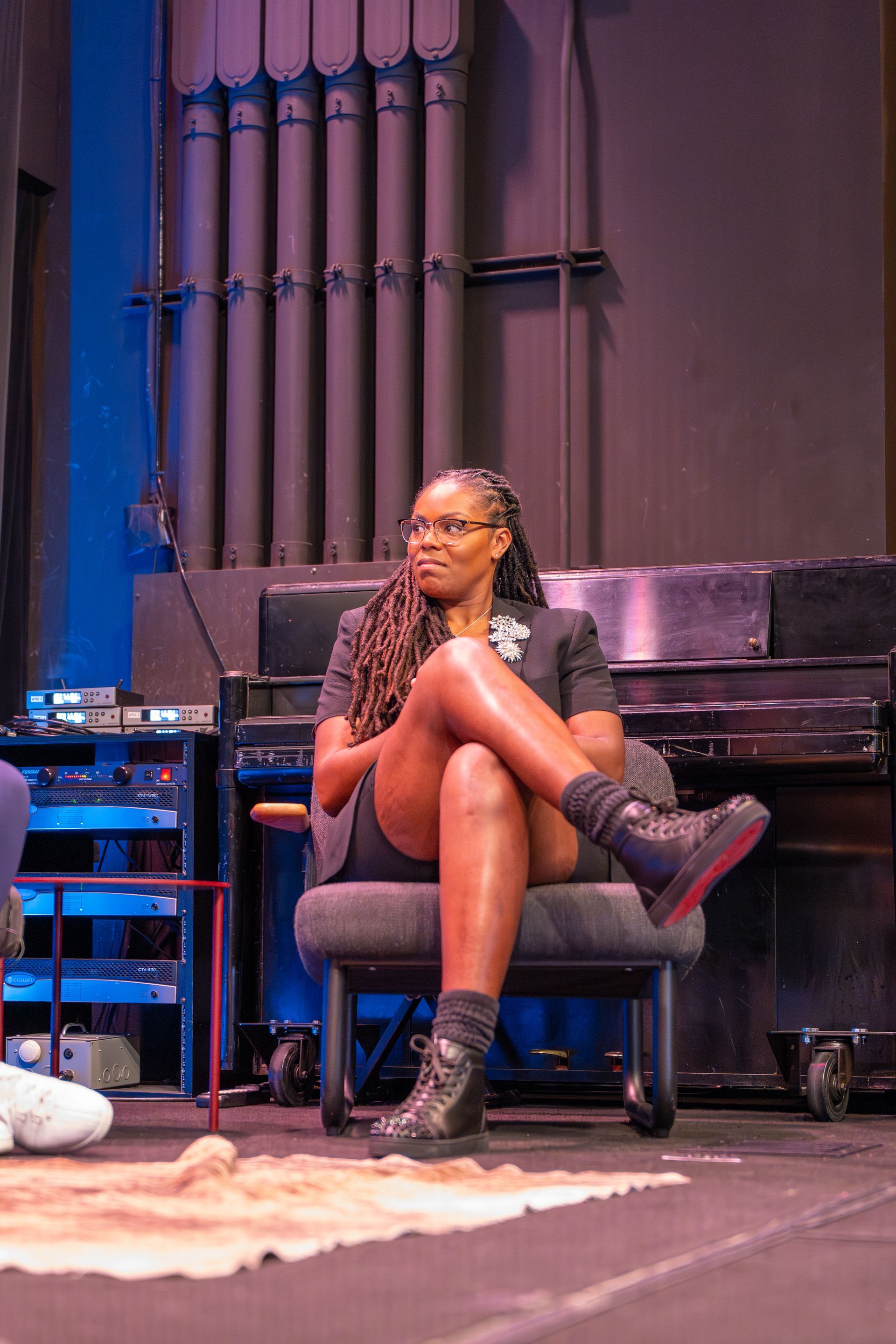 A woman is sitting in a chair on a stage with her legs crossed.