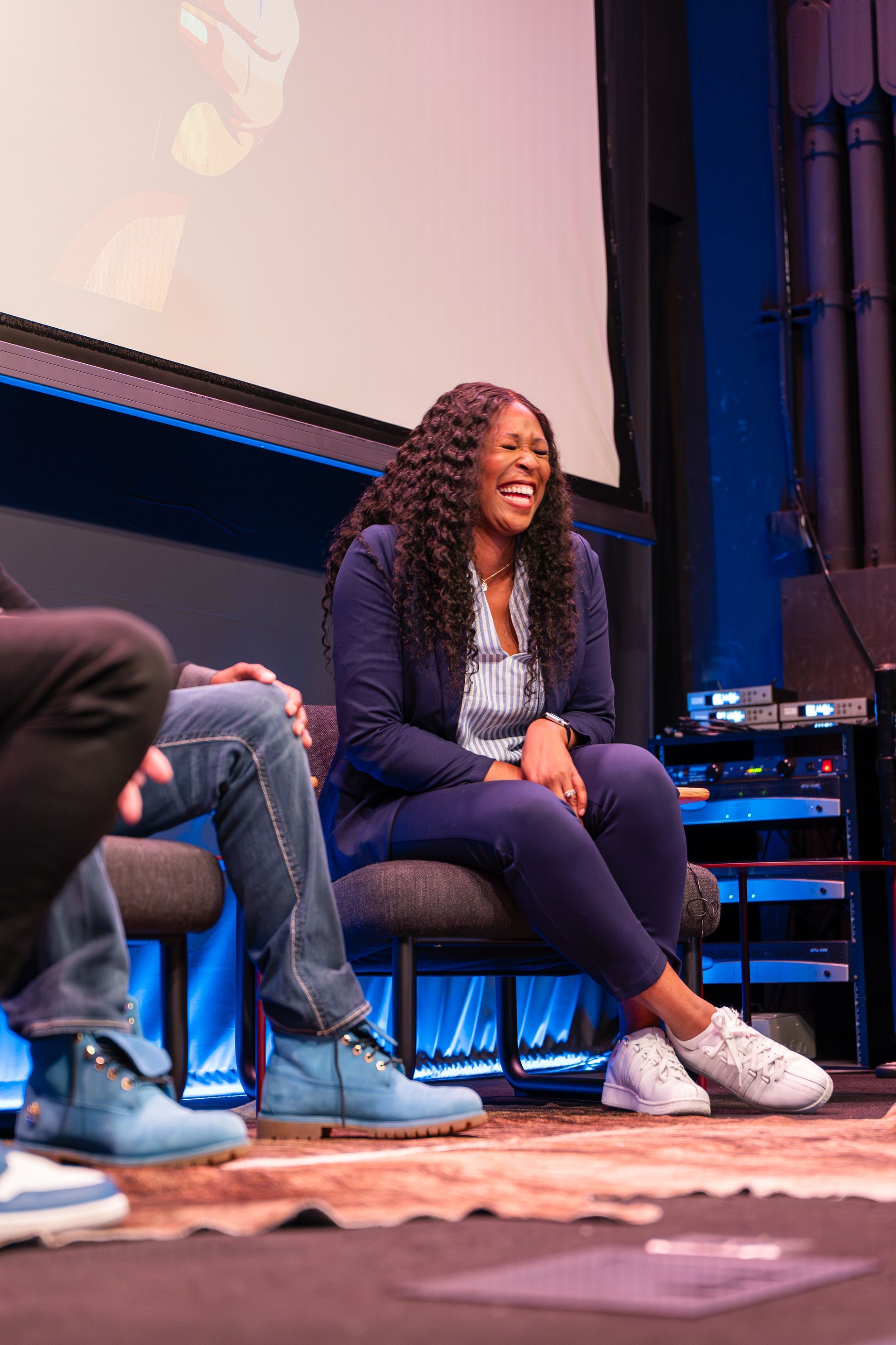 A woman is sitting in a chair on a stage laughing.