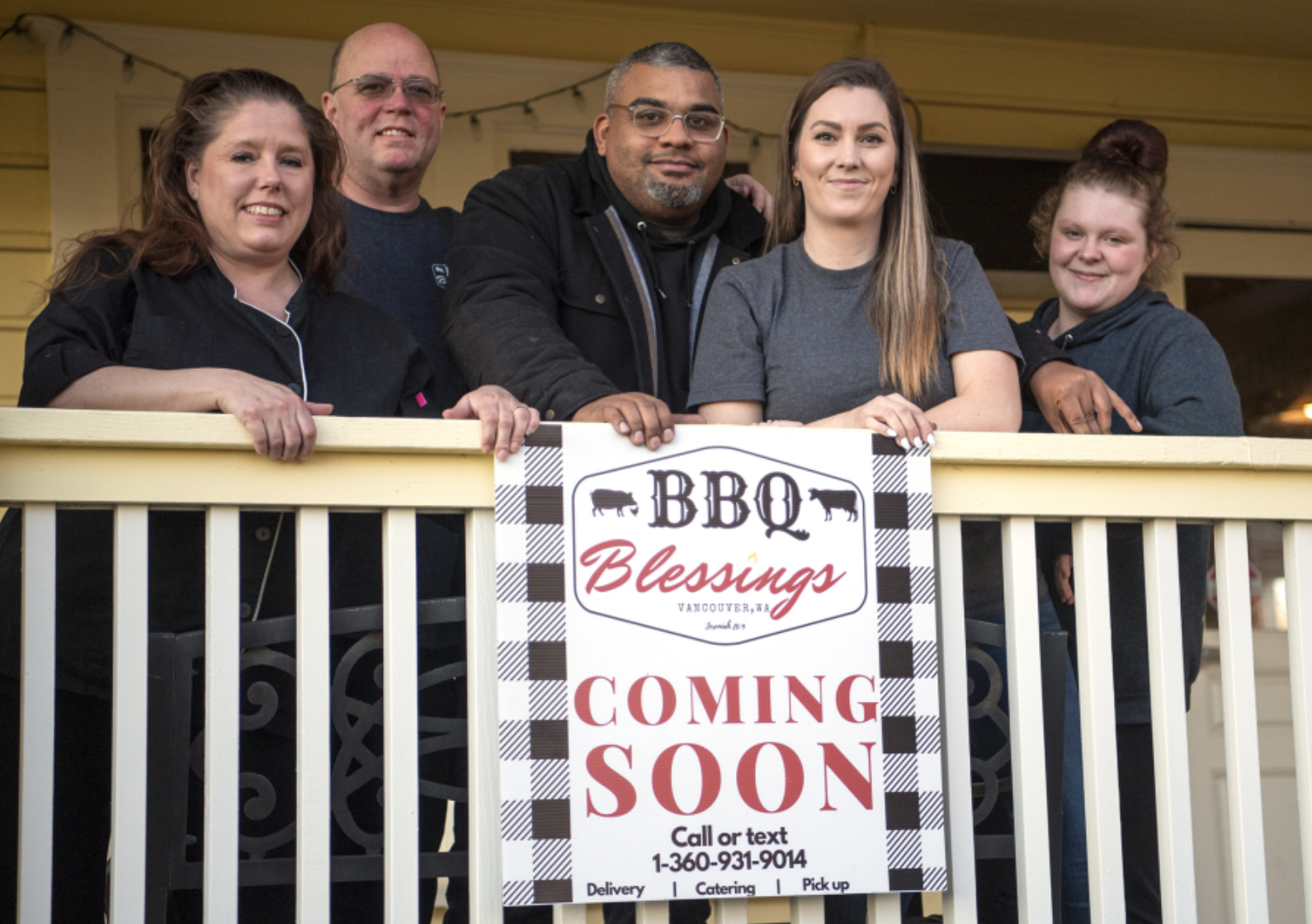 A group of people standing on a porch holding a sign that says bbq blessings coming soon.