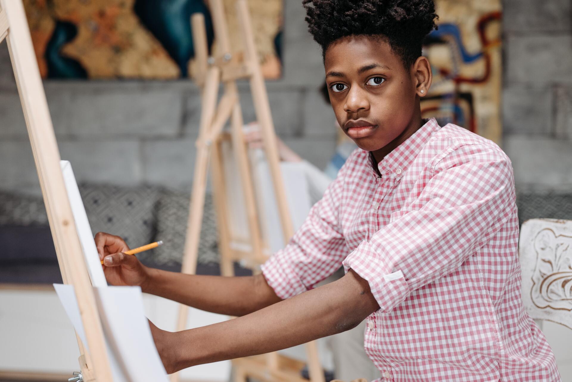 A young man is sitting at an easel painting on a canvas.